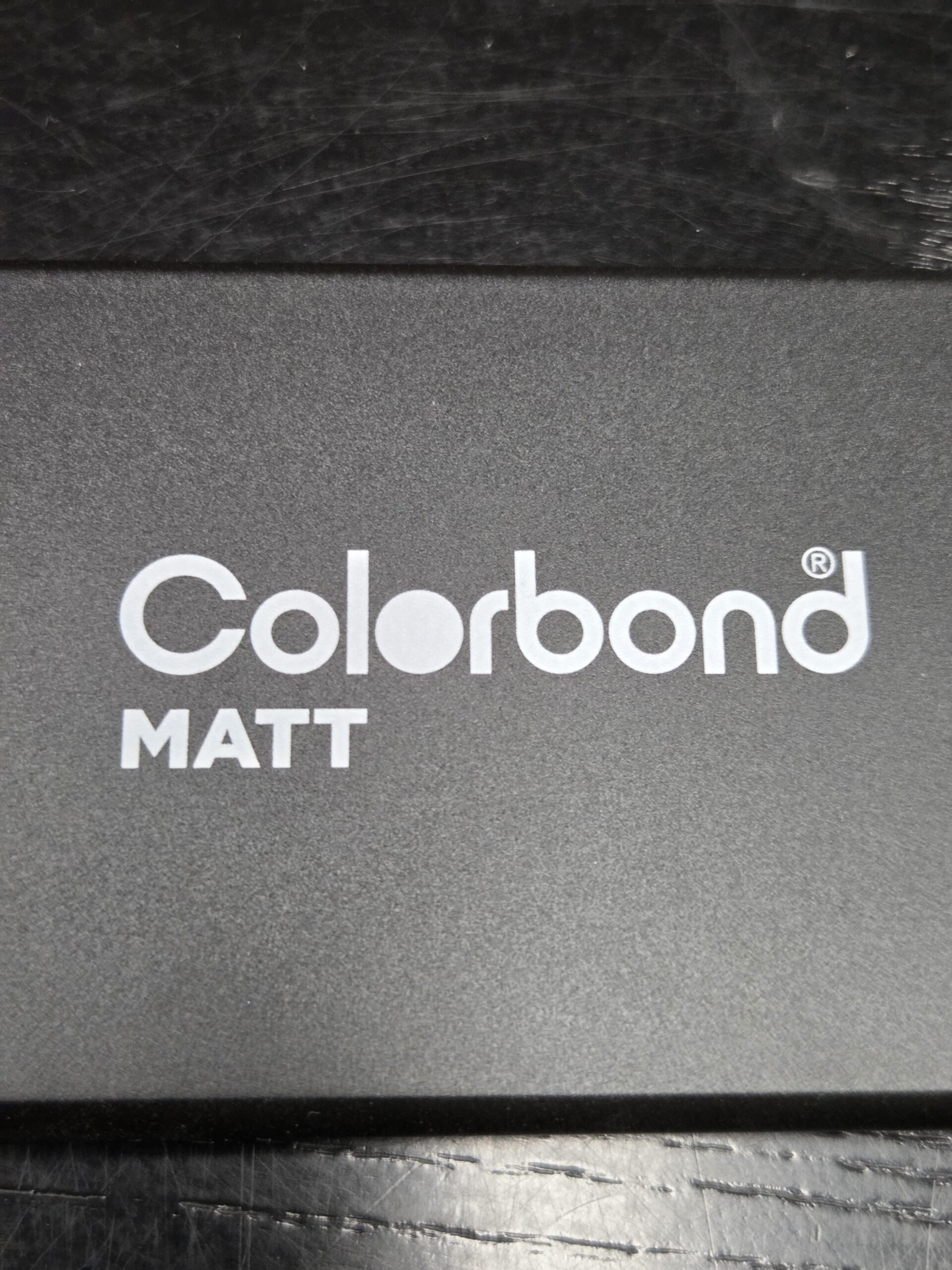 Close-up of the COLORBOND Matt logo on a black textured surface.