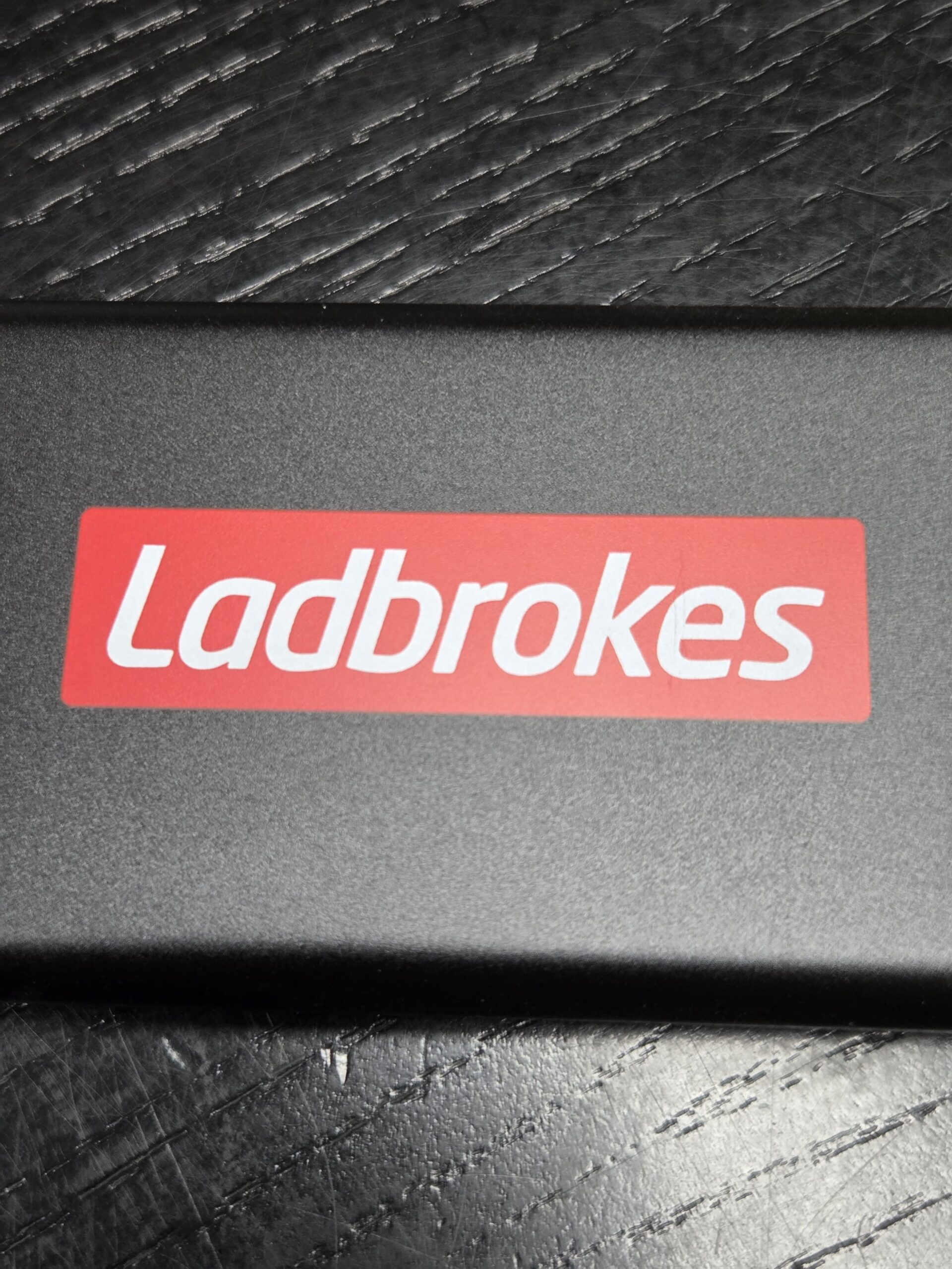 Rectangular object with a red Ladbrokes logo on a textured black surface.