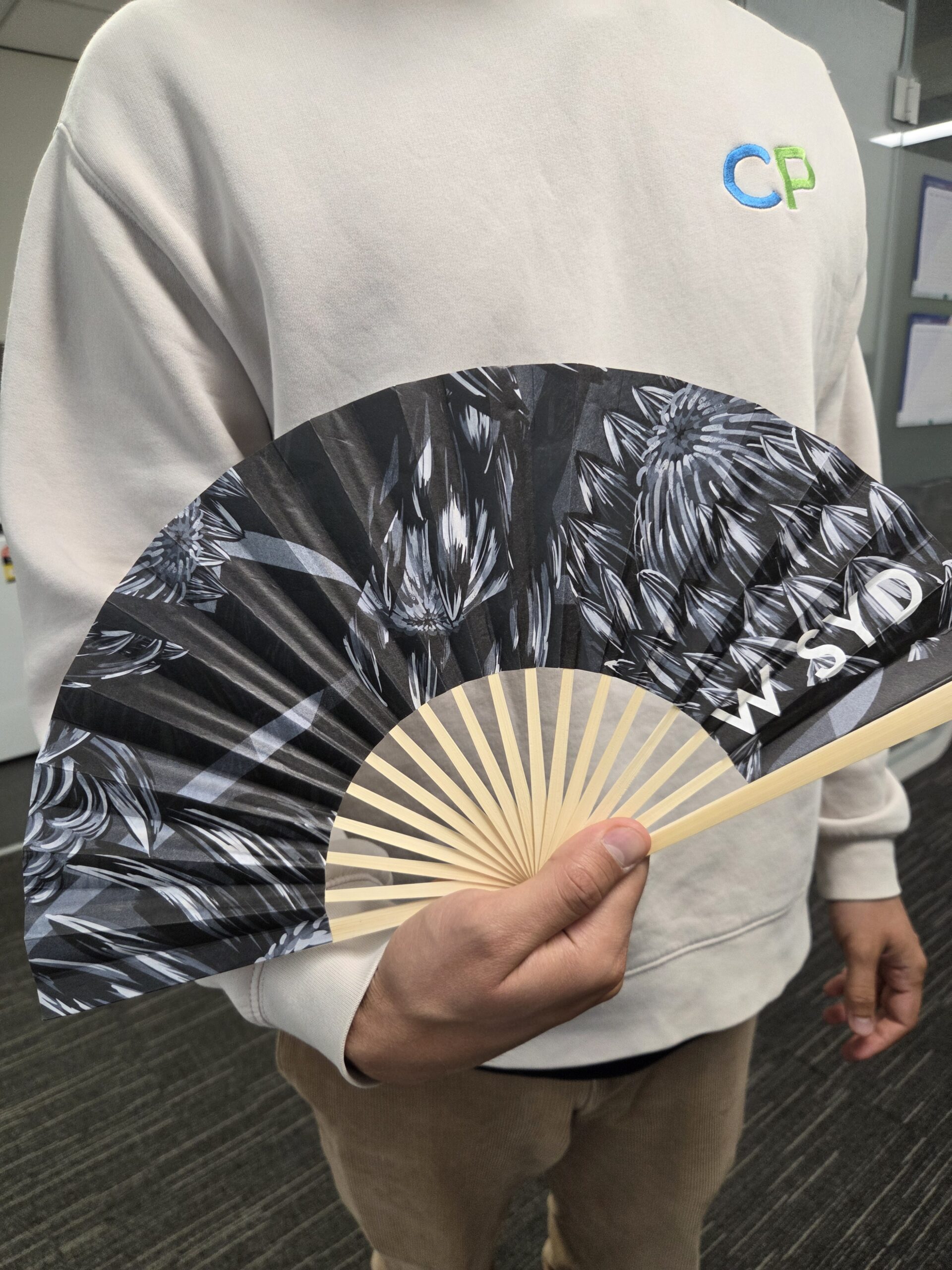 Person in a light sweatshirt holding an open black and white decorative hand fan.