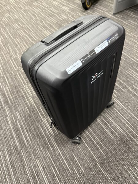 Black hard-shell suitcase, ideal for corporate gifts, on a brown patterned carpet indoors.