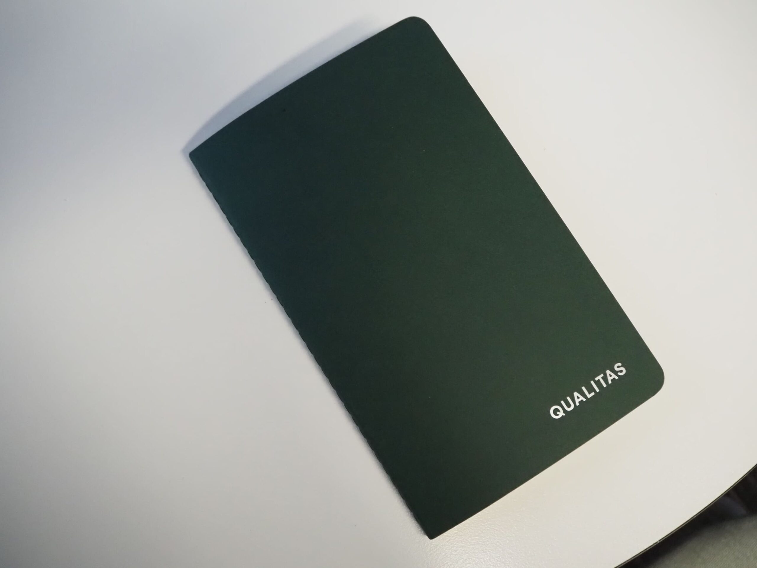 A dark green Qualitas notebook ensuring a Happy Client, set on a white surface.