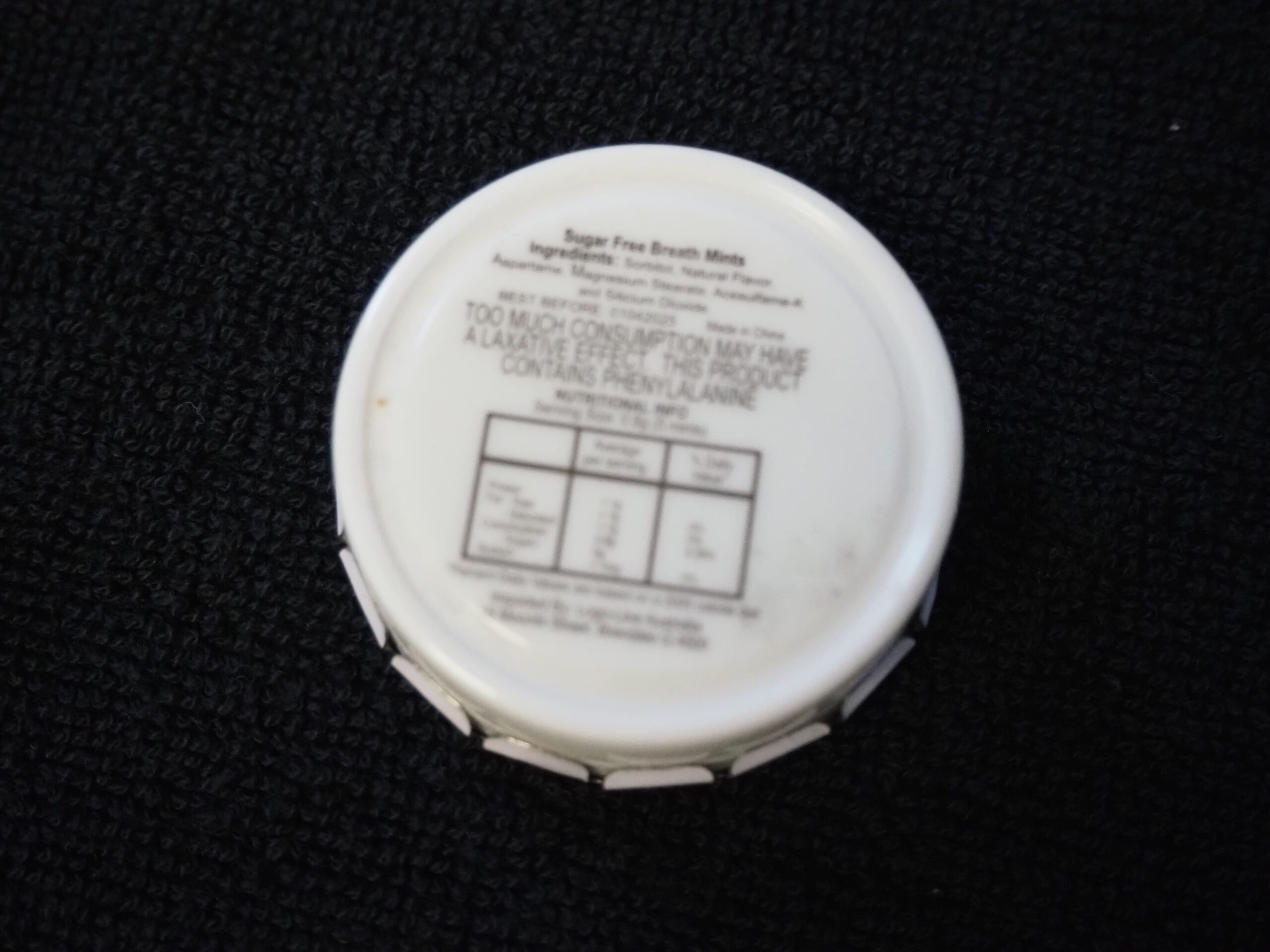 Round white mint container with Fraxtor Australia label and nutrition facts, on a dark surface.