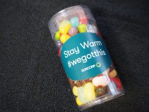 Clear lolly container filled with colourful jelly beans, labelled “Stay Warm #wegotthis” with the Suncorp logo.