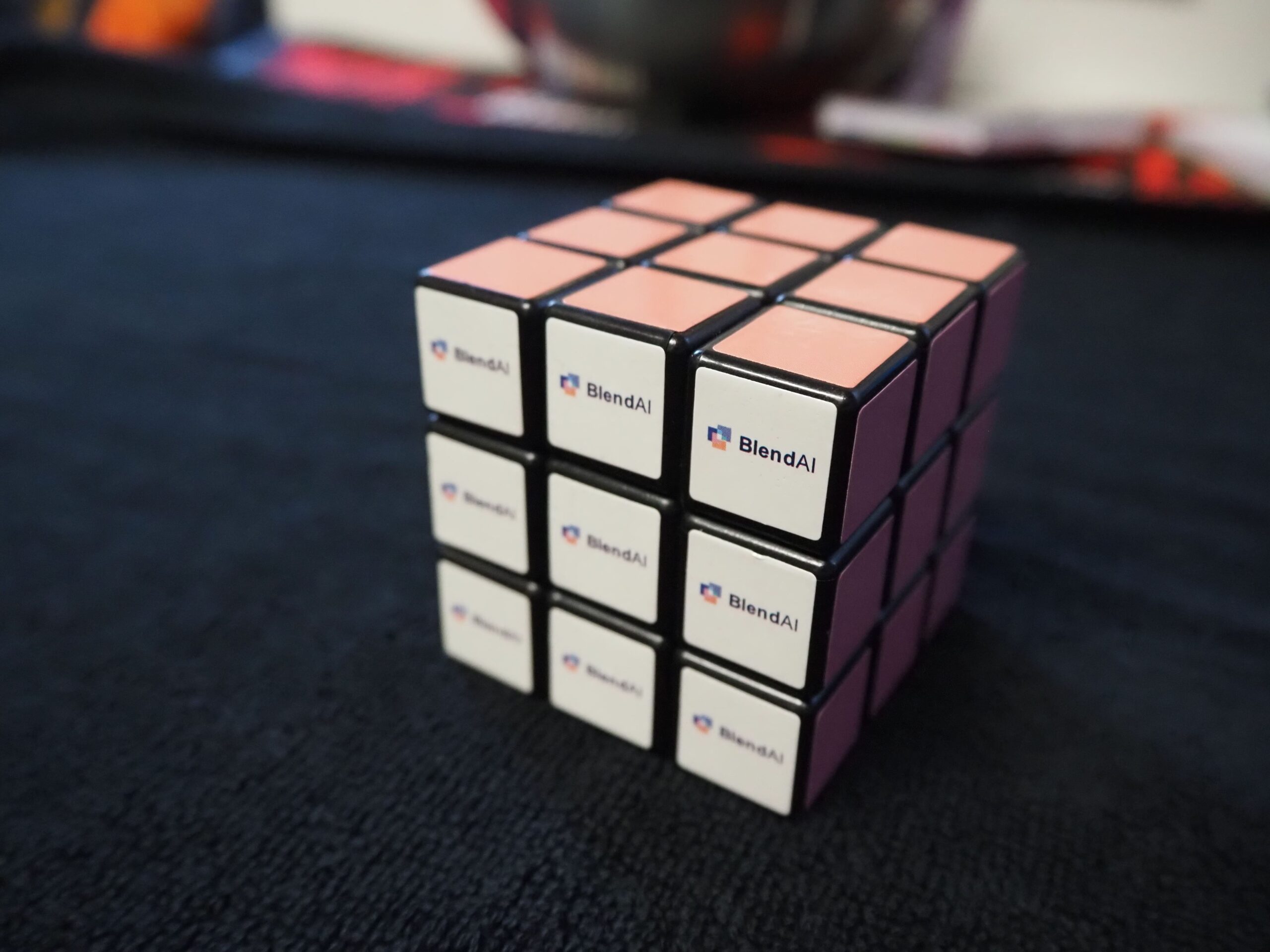A Rubik’s cube with pink sides and Blend AI logos, on a dark surface.
