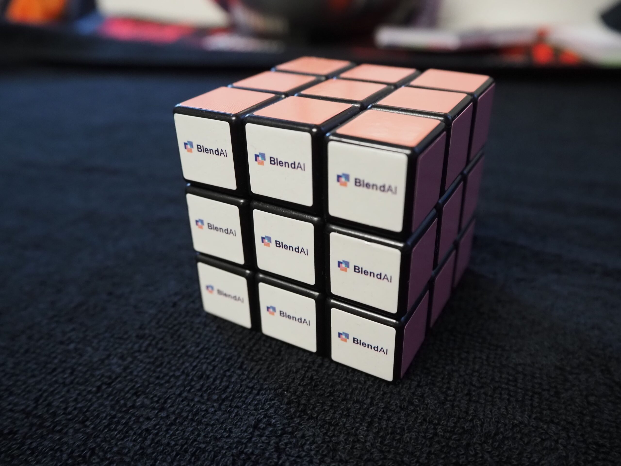 A Rubik’s Cube with Blend AI logos on each white sticker, placed on a dark surface. Client Story.