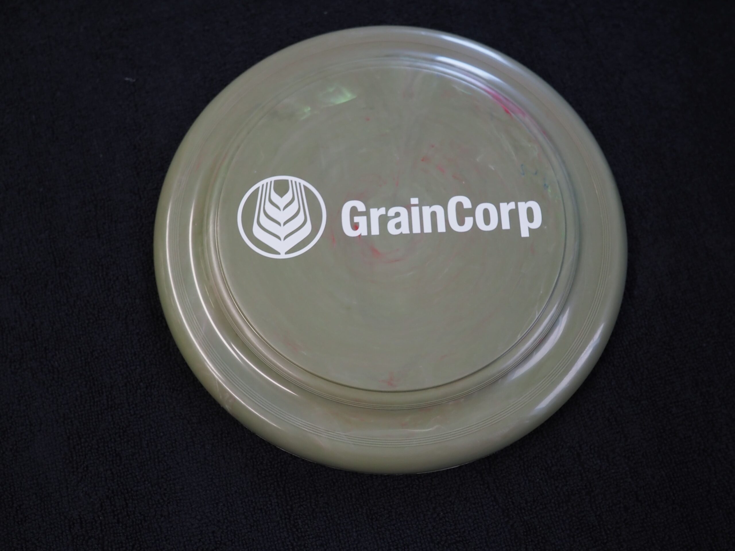 A khaki frisbee with the GrainCorp logo, perfect for a fun client story on a black surface.