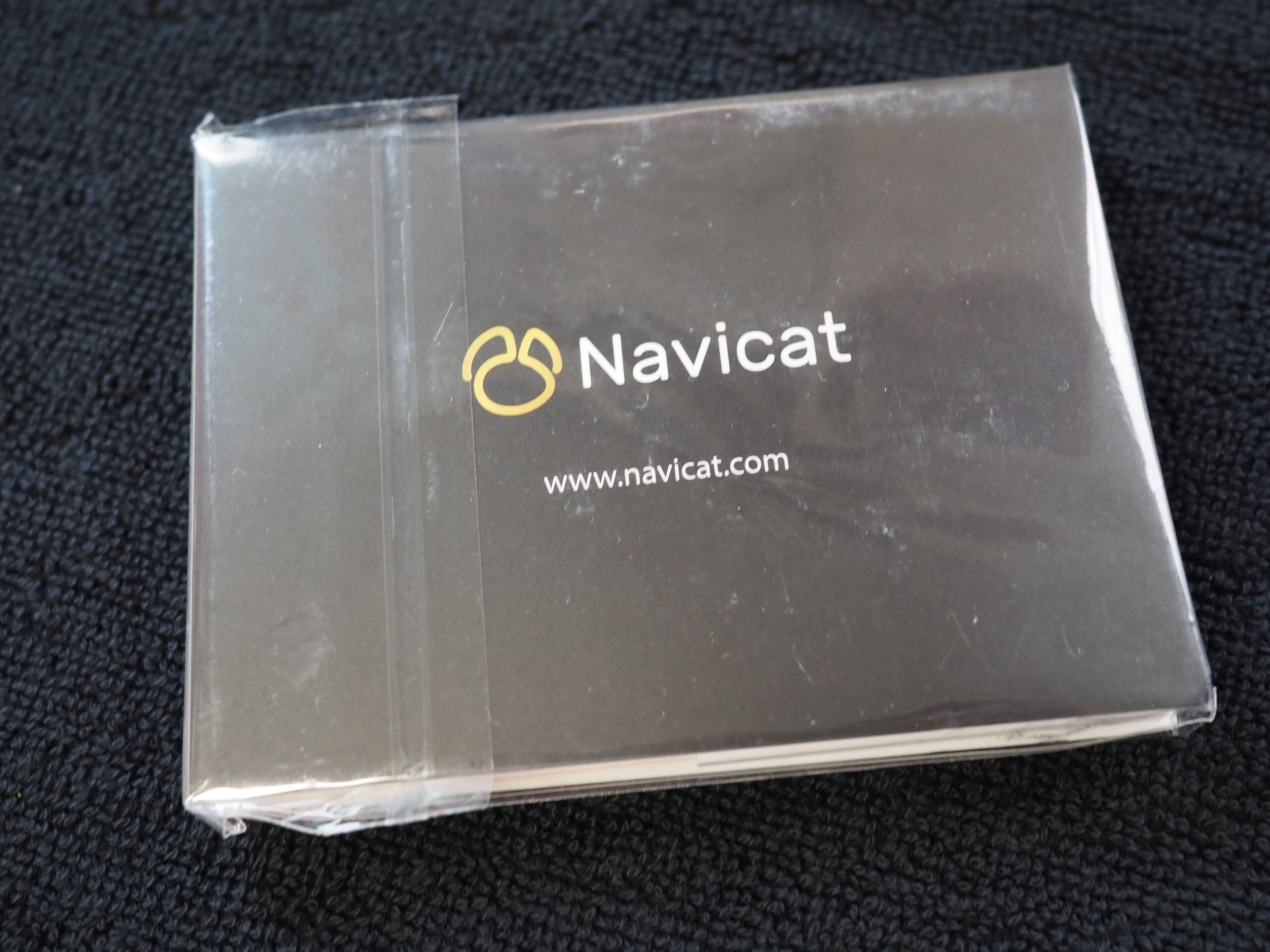 A plastic-wrapped Navicat card for database management on a dark fabric surface.