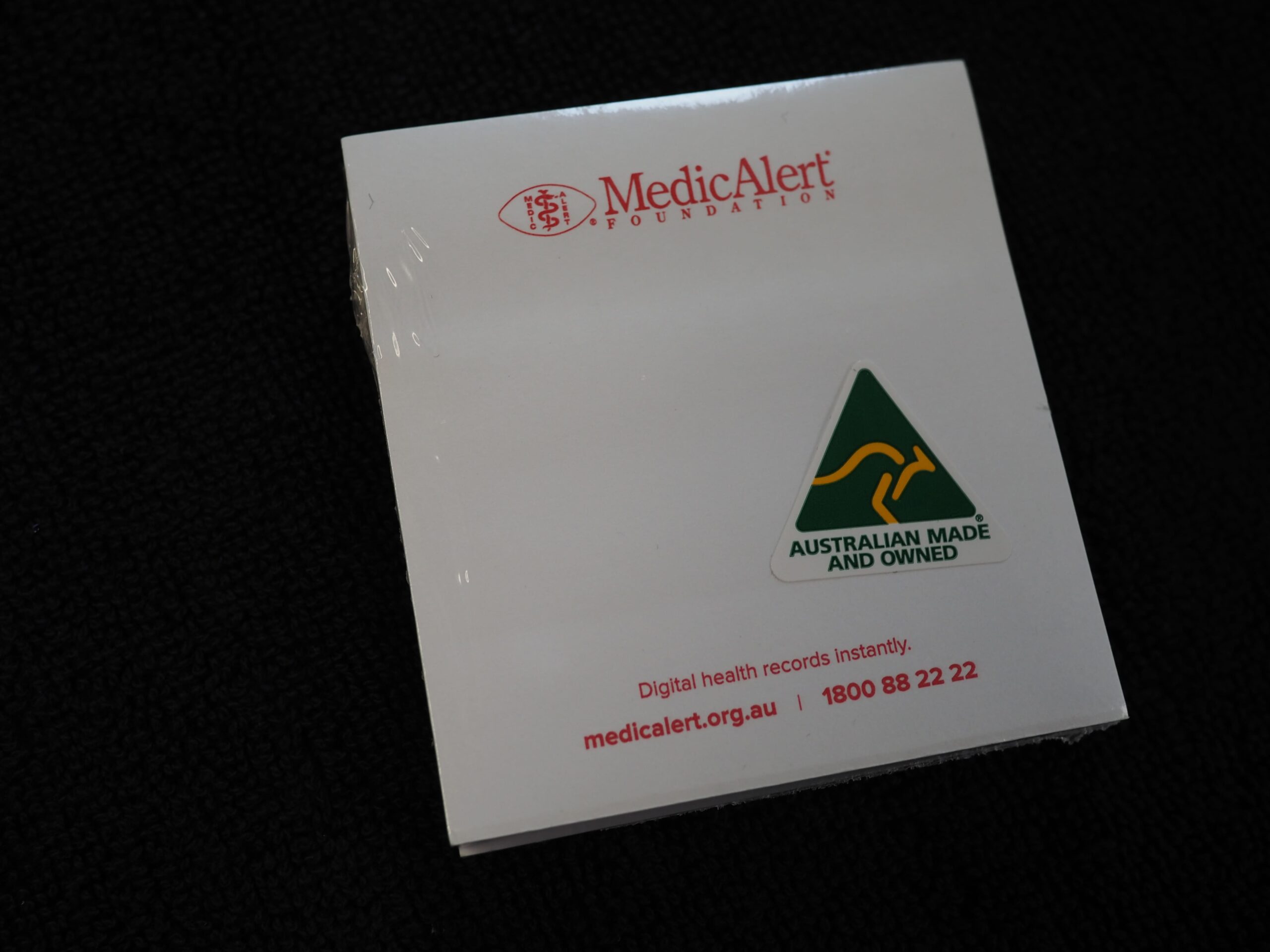 White MedicAlert notepad with medical ID and Australian Made and Owned logo on black background.