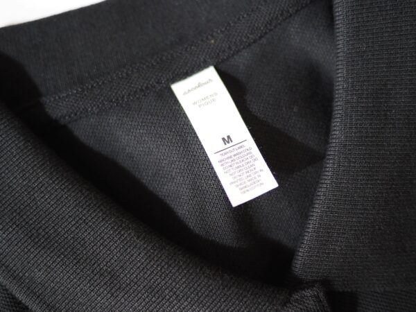 Close-up of a black polo shirt collar with a visible size M tag inside.