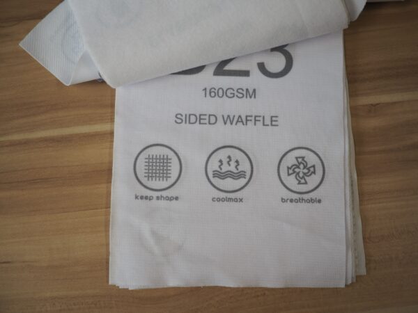 White polo fabric sample with icons for keep shape, coolmax, and breathable features.
