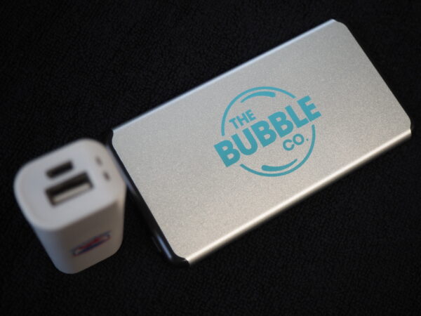 A travel-friendly USB charger and silver power bank labeled The Bubble Co. on a black surface.