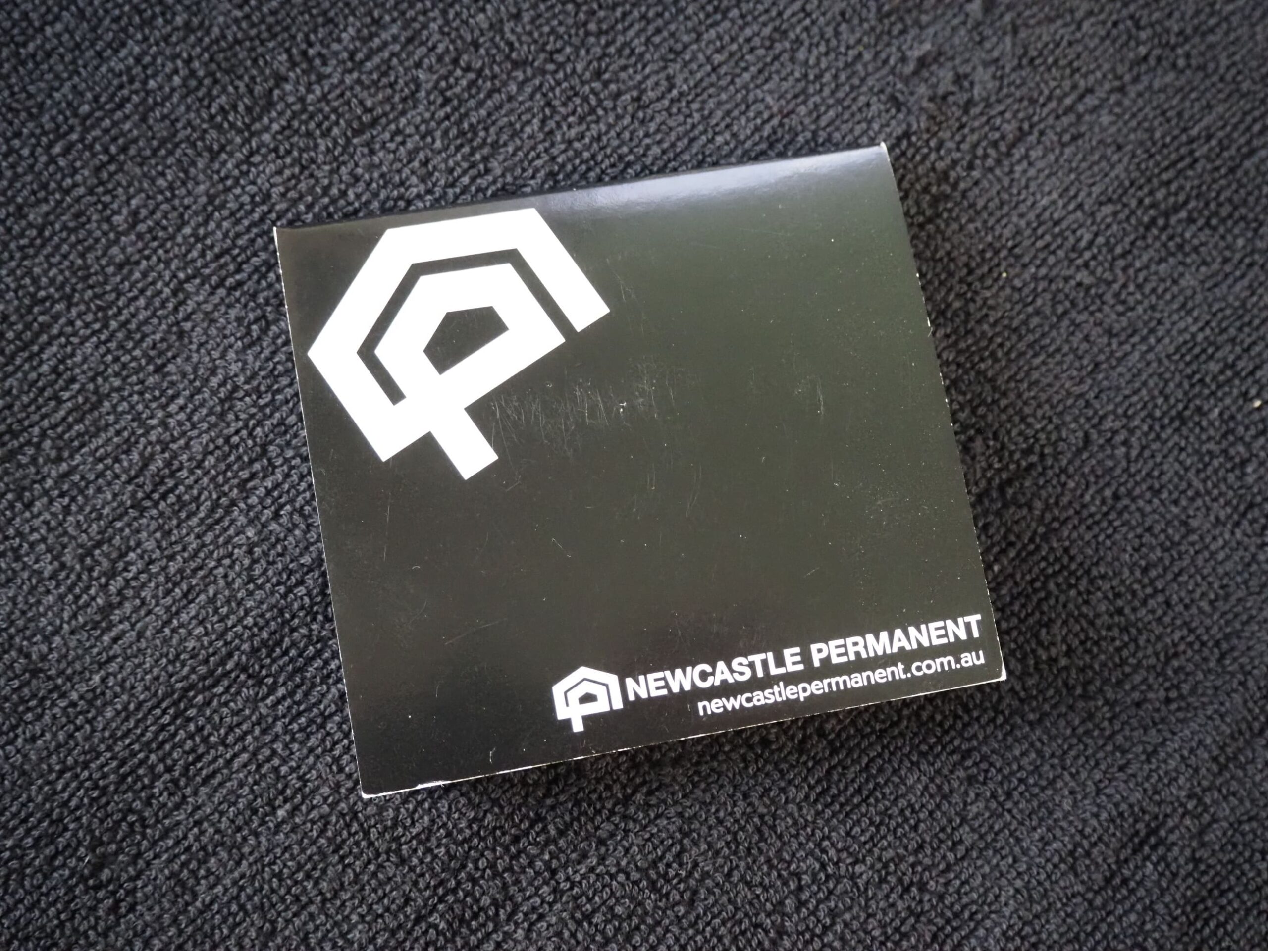 Black box featuring the Newcastle Permanent logo and website on a dark textured surface.