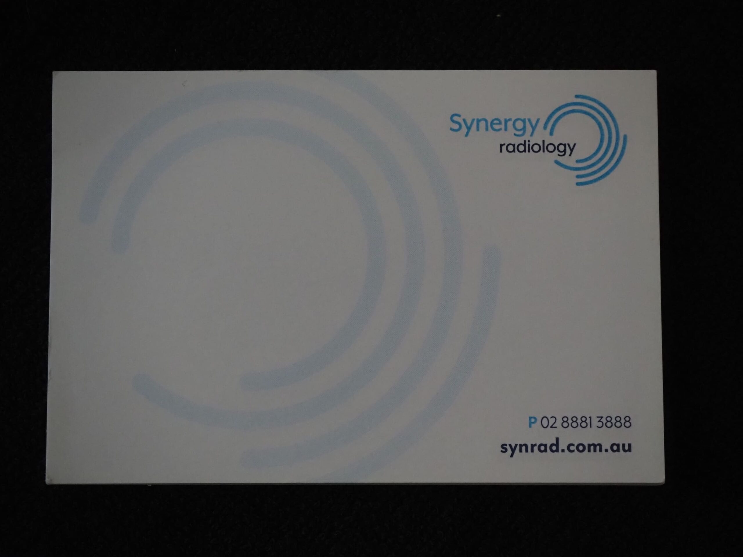 Synergy Radiology business card with contact info, blue circular design for radiology services.