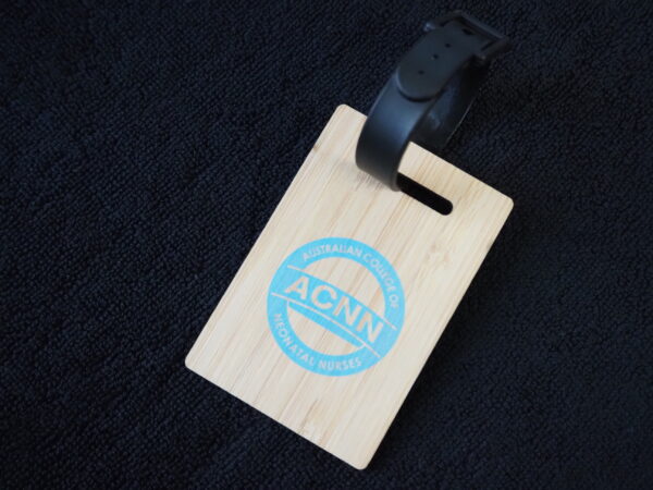 Wooden luggage tag with ACNN logo—perfect for corporate gifts—on a dark fabric background.