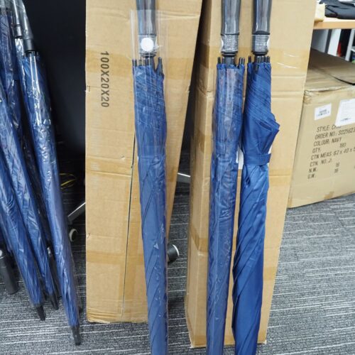 Four blue umbrellas, ready for placing an order, lean against boxes on a carpeted floor.
