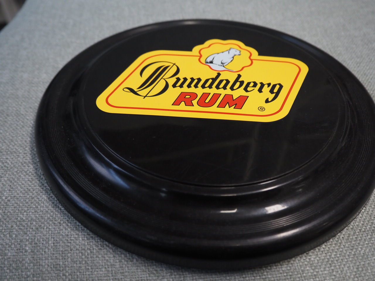 A black Bundaberg Rum frisbee rests on a grey fabric surface.