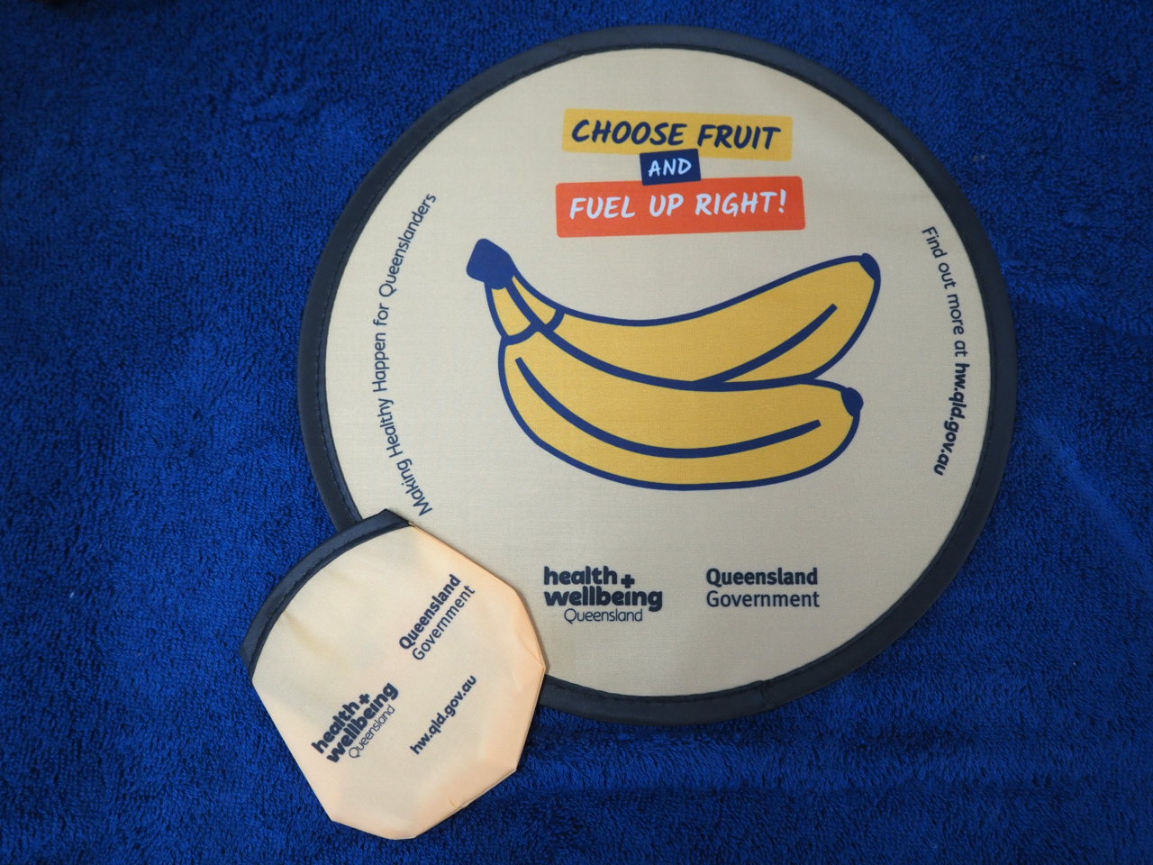 Round frisbee with cartoon bananas, health slogan, Era Polymers logo, on blue fabric and pouch.