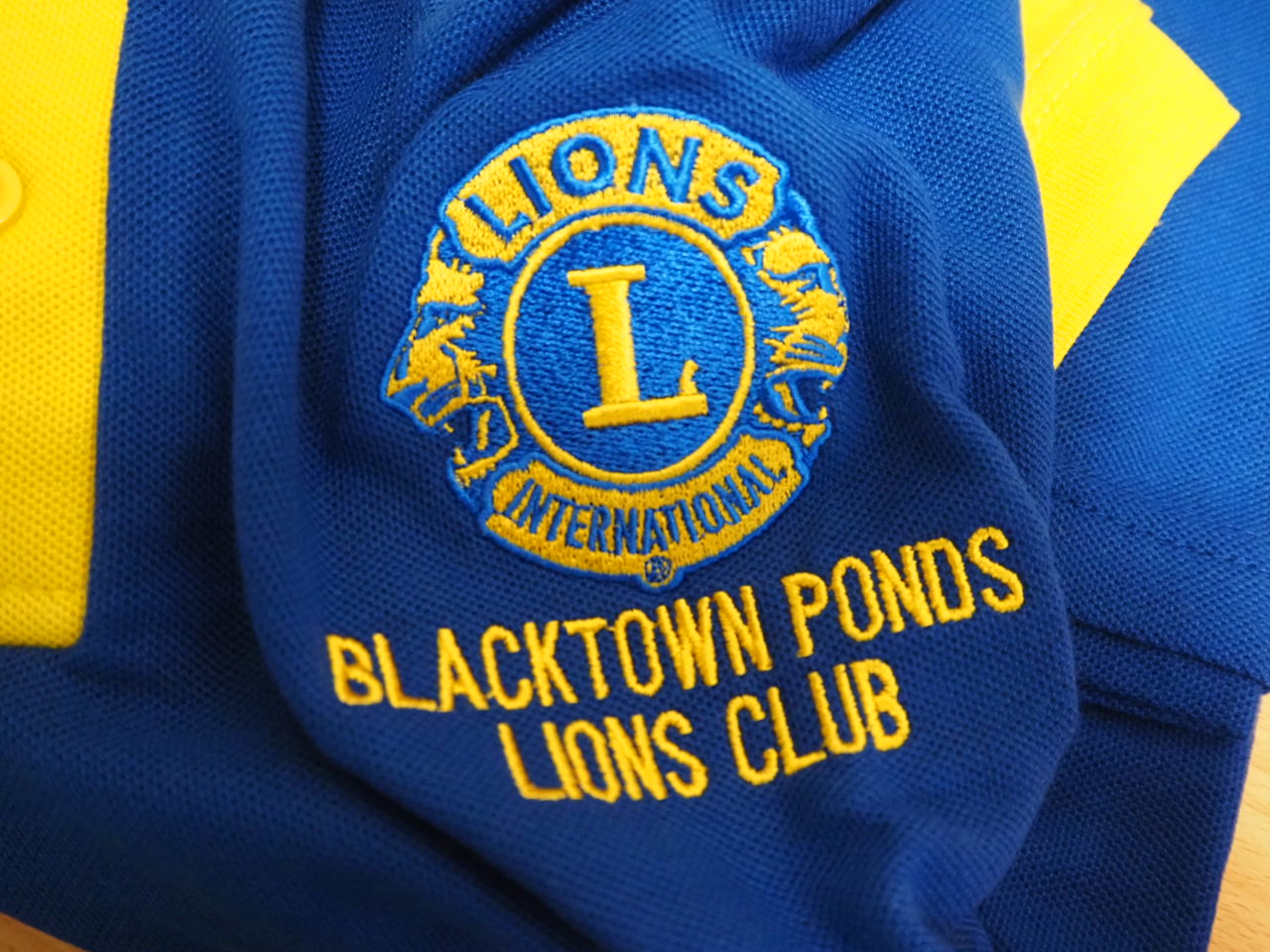 Blue and yellow Lions Club shirt with Blacktown Ponds Lions Club embroidered logo.