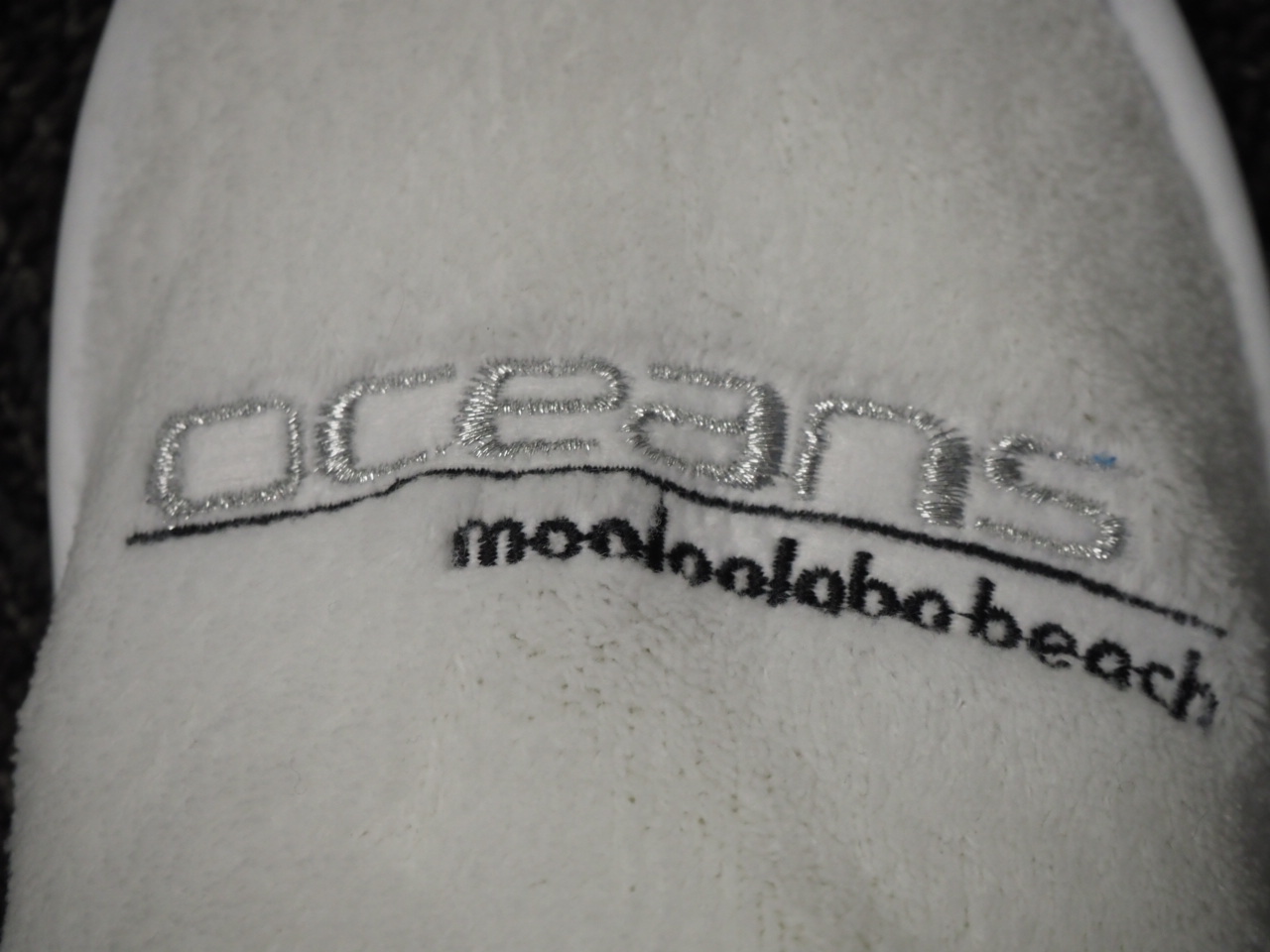 White fabric with silver embroidery reading Oceans Mooloolaba on it.