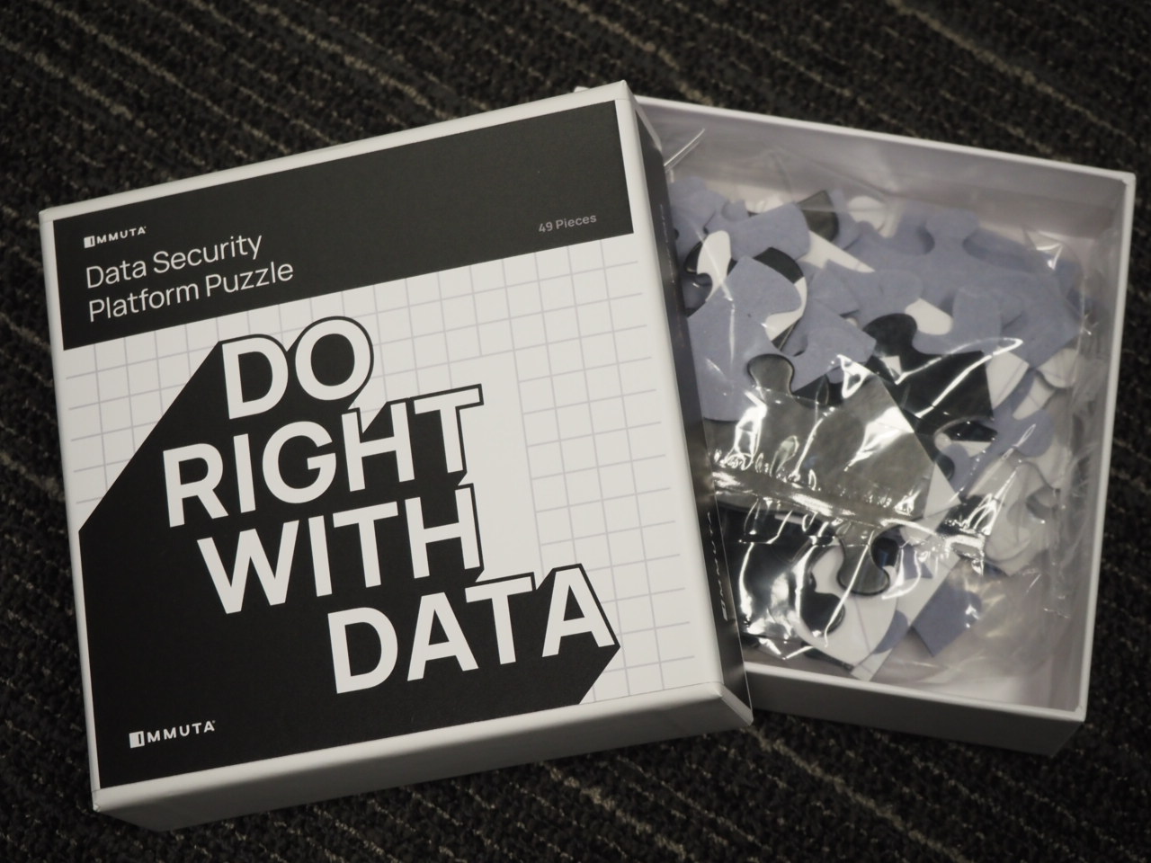Box labeled DO RIGHT WITH DATA by Immuta sits beside an open puzzle bag on a carpeted floor.