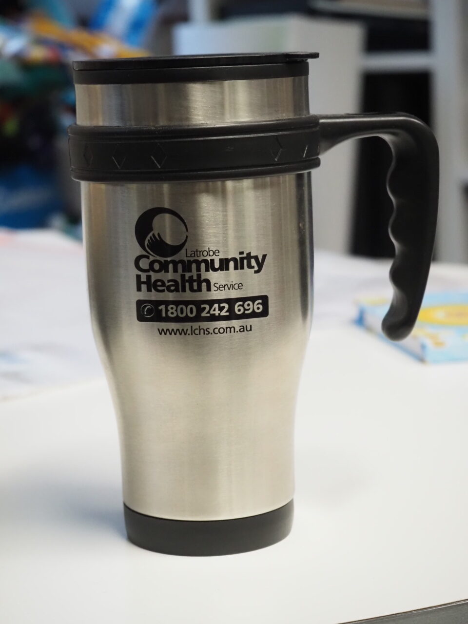 A stainless steel travel mug featuring the Latrobe Community Health Service logo.