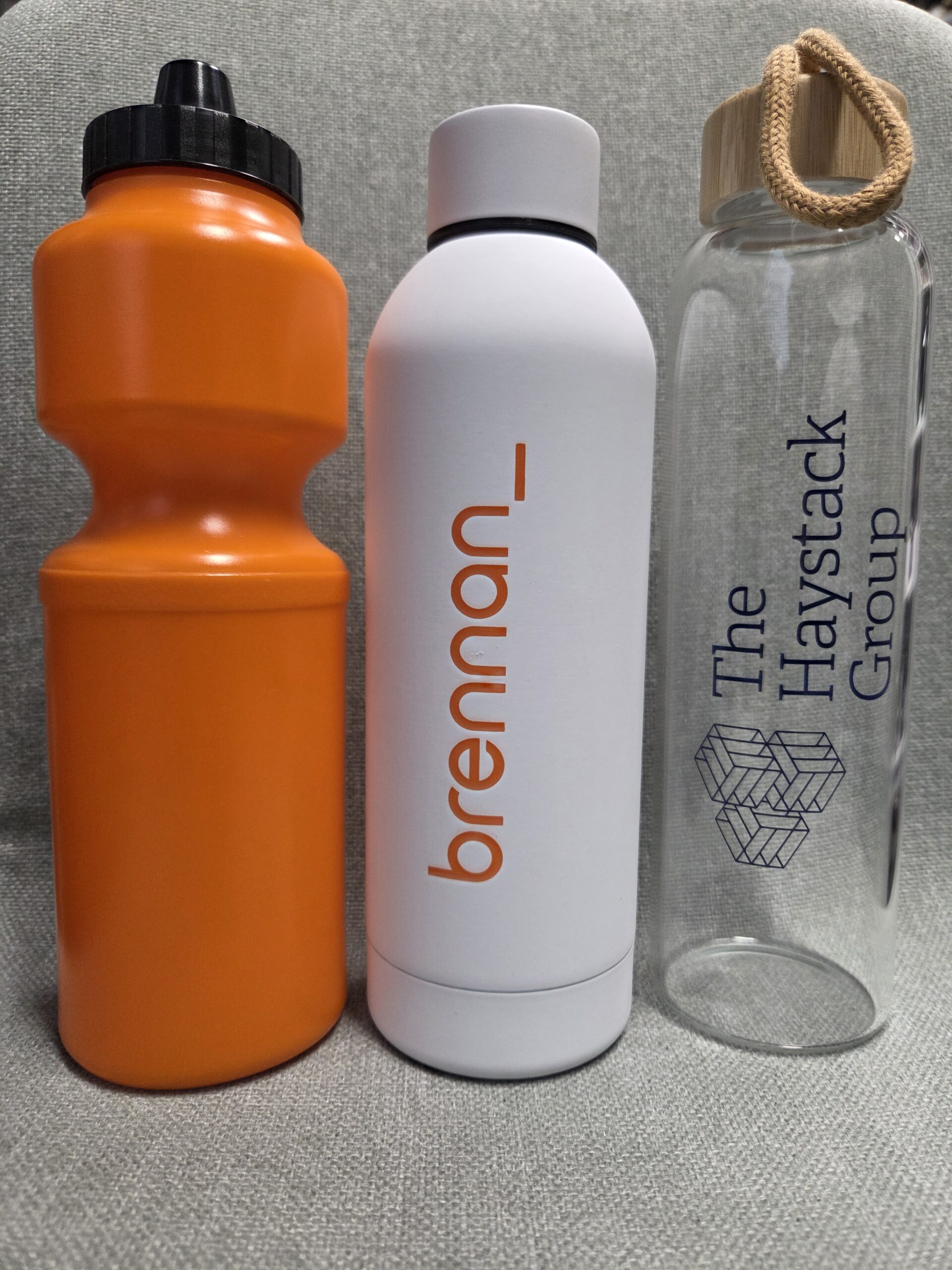 Three water bottles—perfect as Christmas gifts: orange, white with brennan_, and clear Haystack Group.