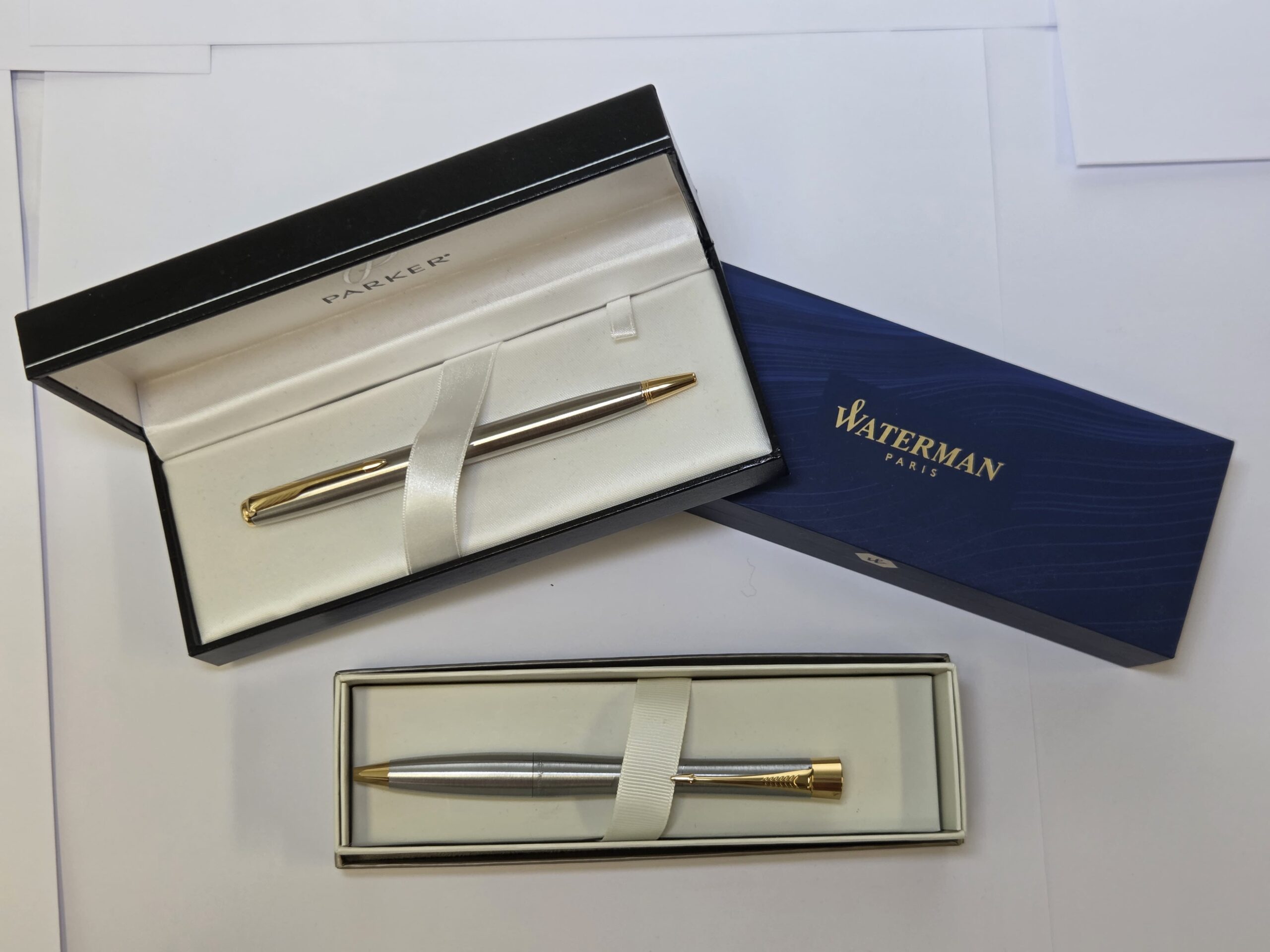 Two luxury pens in open boxes, perfect gifts from Parker and Waterman on a white surface.