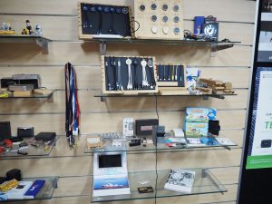 Glass shelves displaying electronics, gadgets, and rebrand-themed lanyards on a wooden wall.