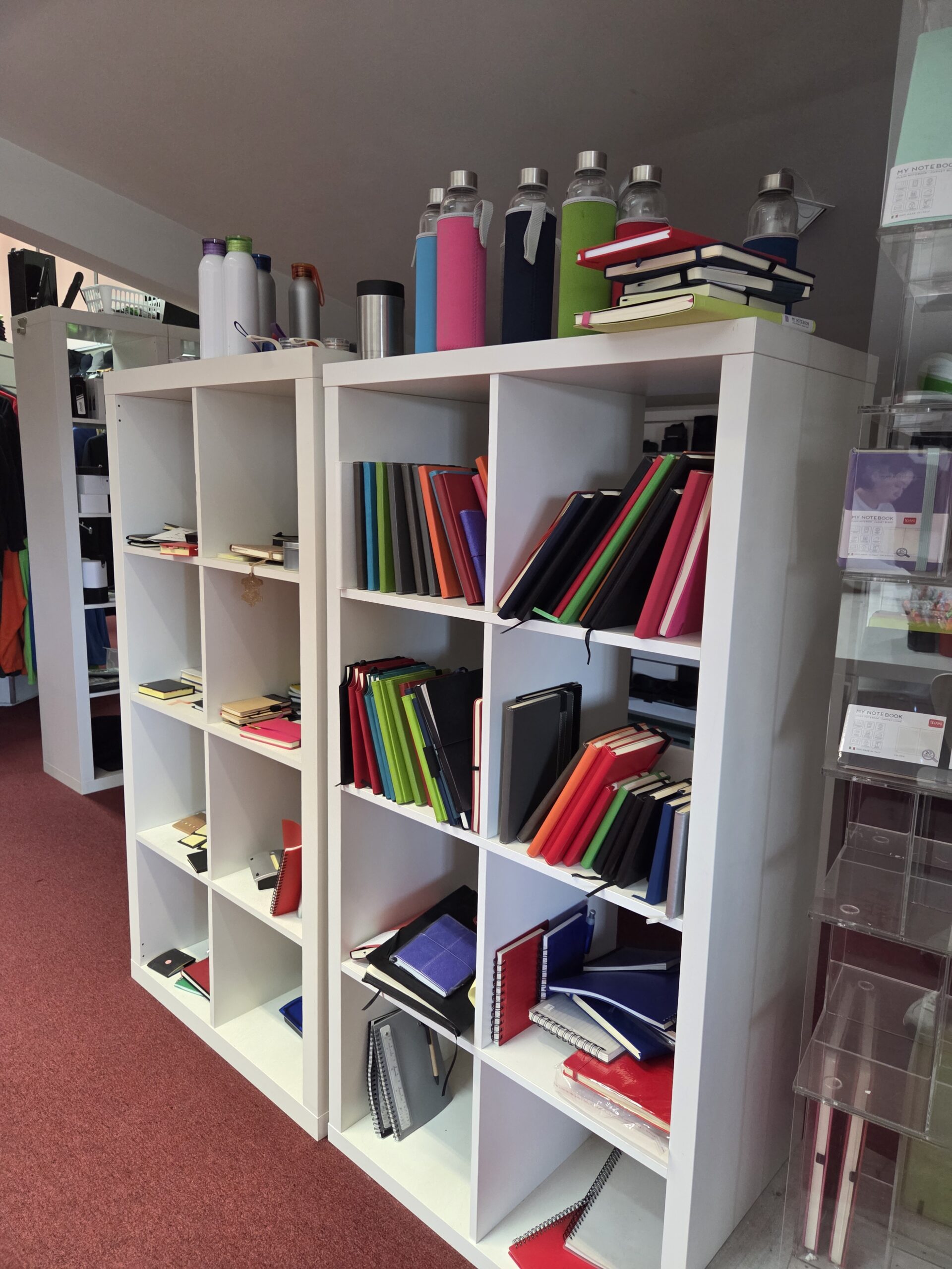 Two white shelves filled with colorful notebooks and bottles in a store setting.