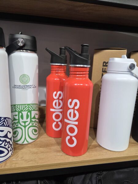 Red Coles drink bottles with white logo, perfect as promotional products, on a wooden shelf.