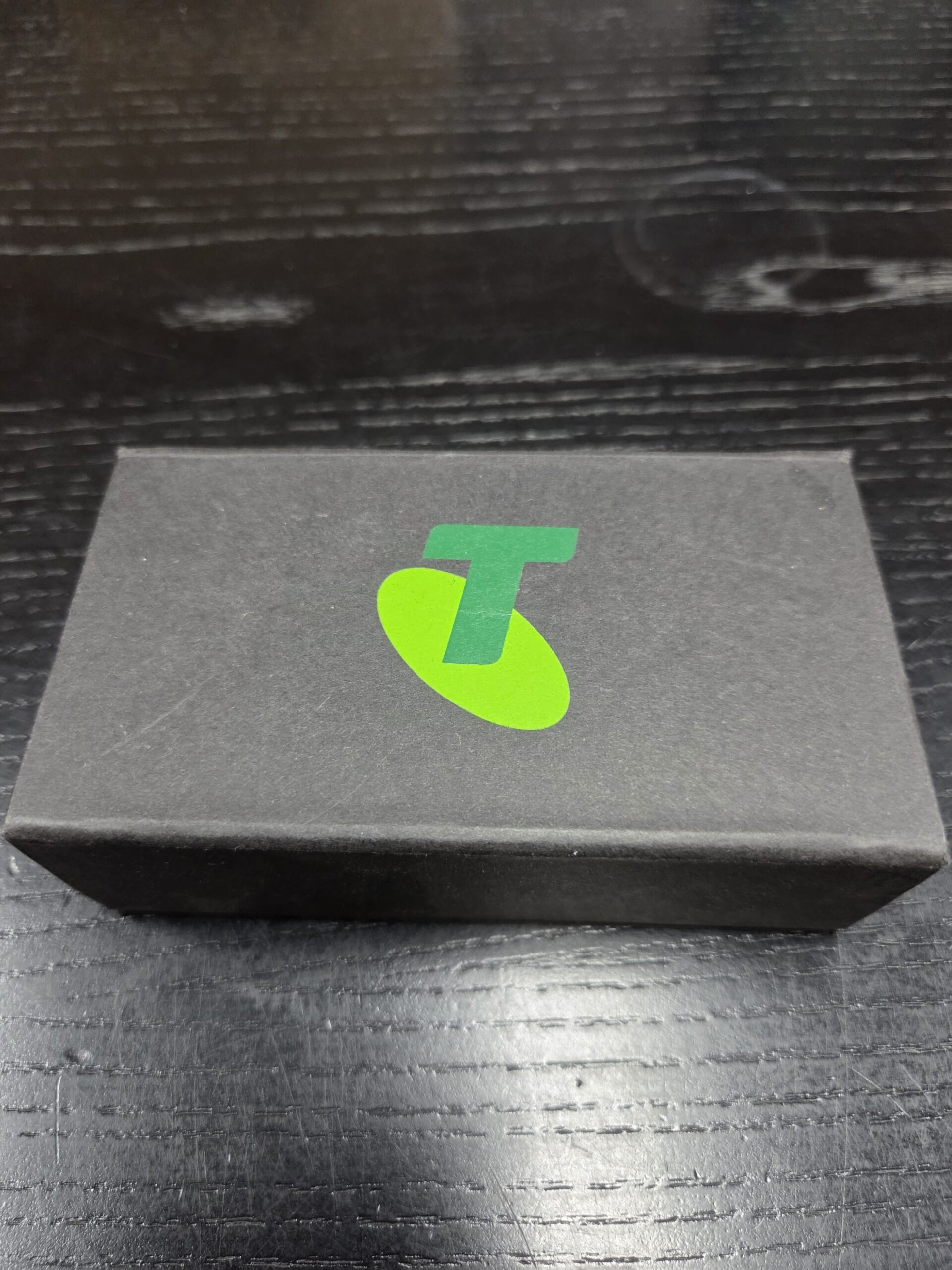 A black Telstra box with a green logo sits on a dark wooden surface—Happy Client Story.