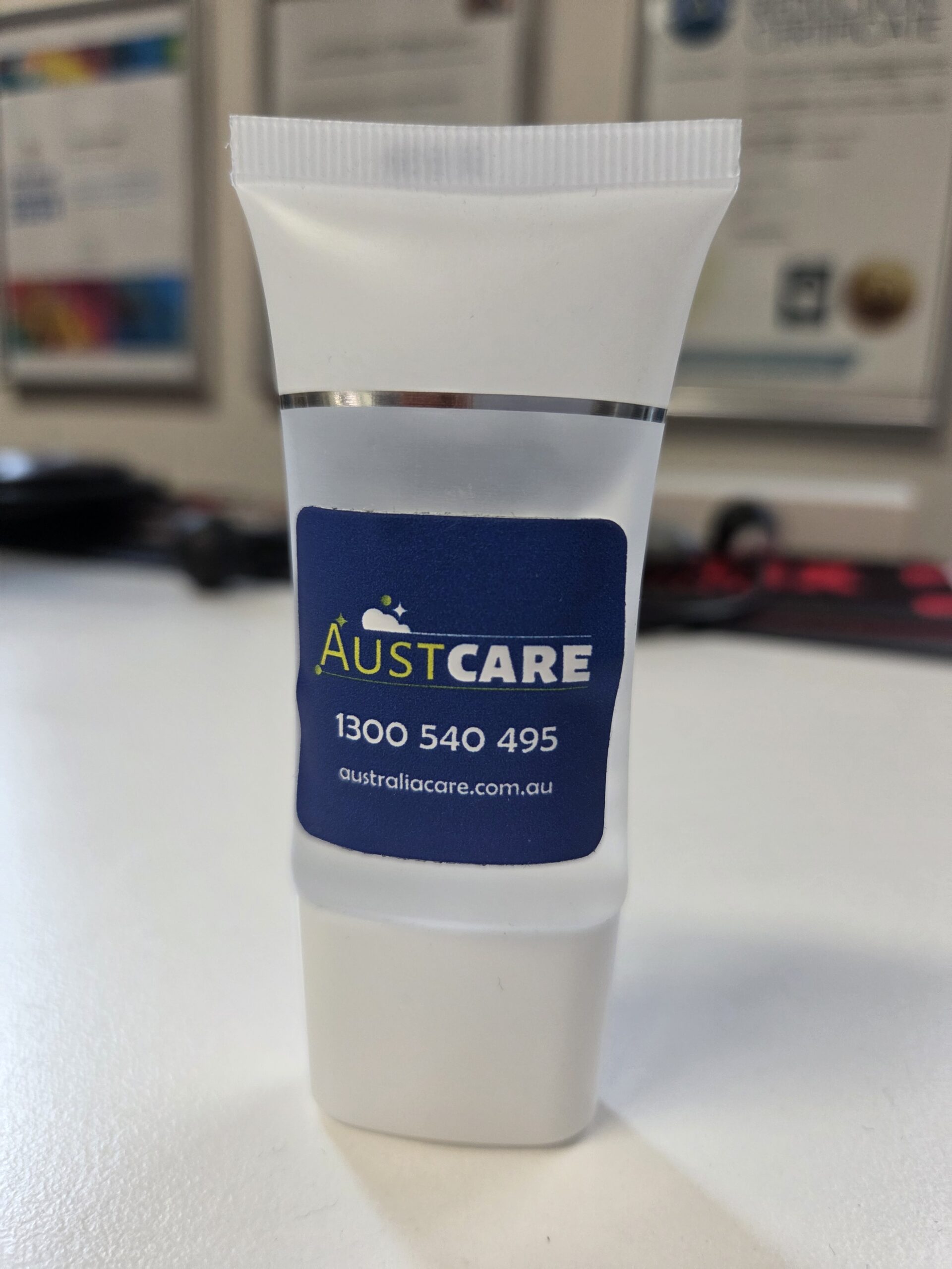 Small white AustCare tube with contact info, featured in a Client Story, on a white surface.