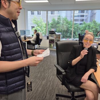 Two coworkers in an office, wearing yellow glasses as fun promotional merchandise.