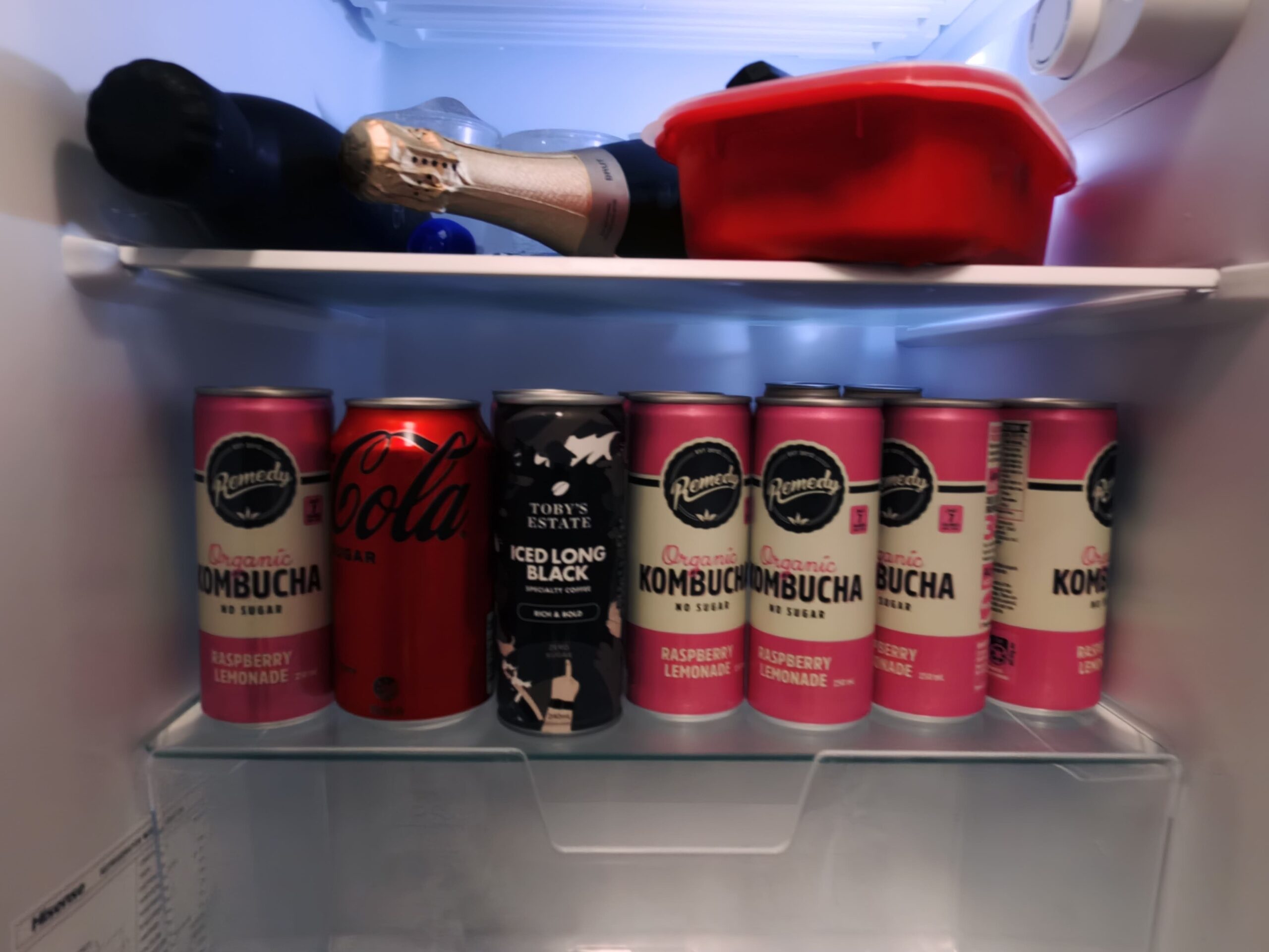 Cans of drinks and champagne in a fridge, like a mini showroom, with a red container above.