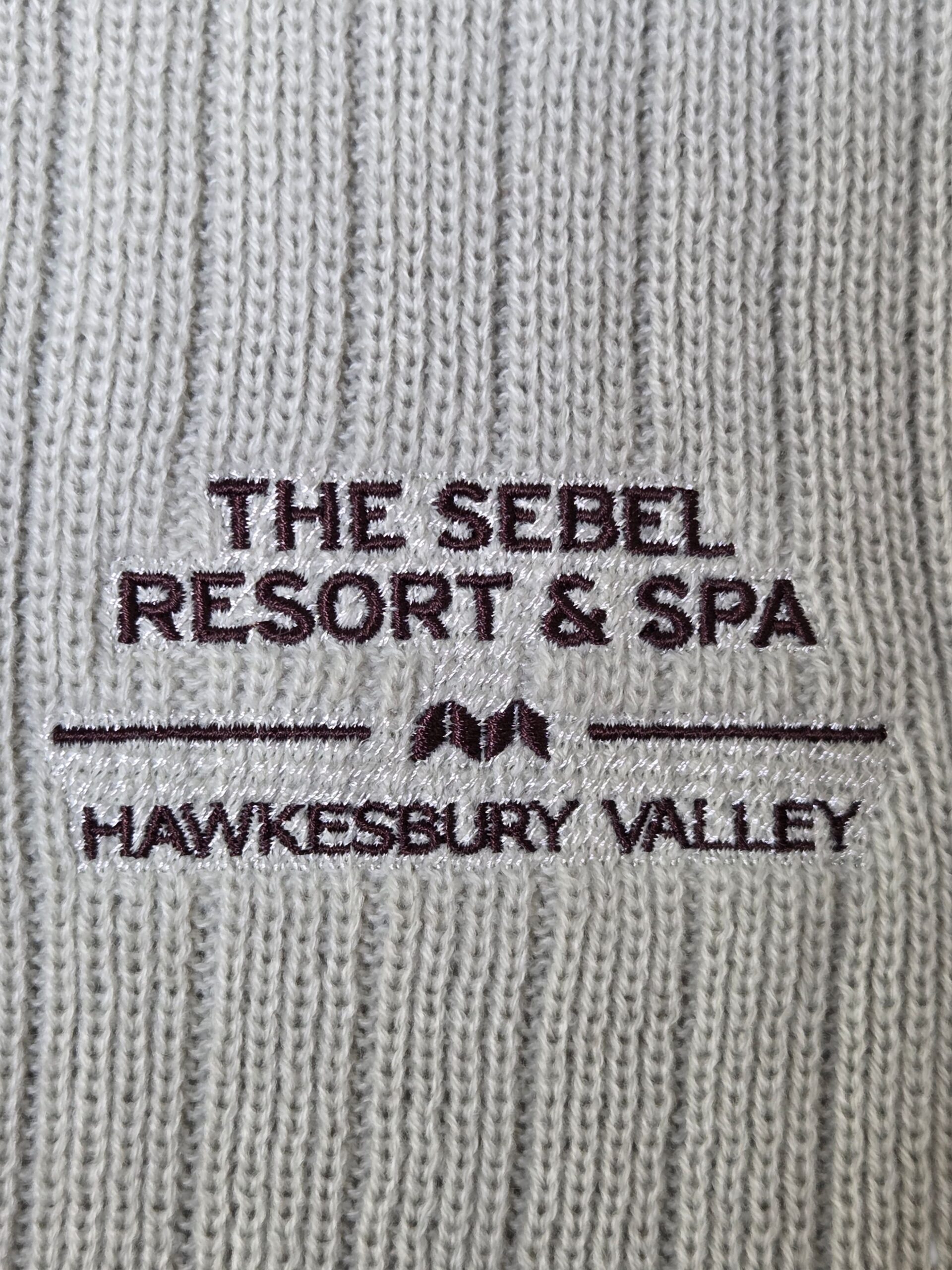Grey knitted fabric with Sebel Resort Hawkesbury Valley embroidered in brown.
