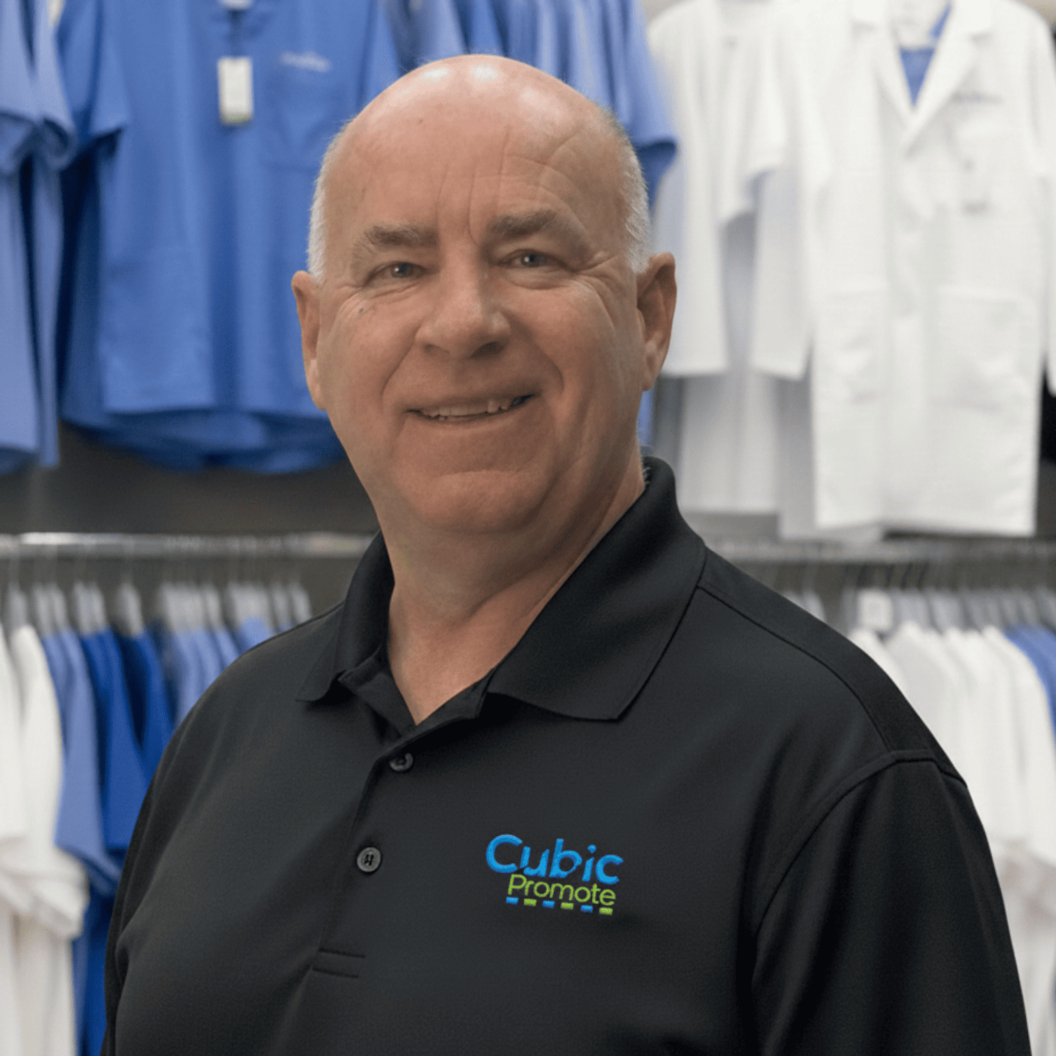 Meet the team: Smiling man in a black Cubic Promote shirt stands before racks of clothing.