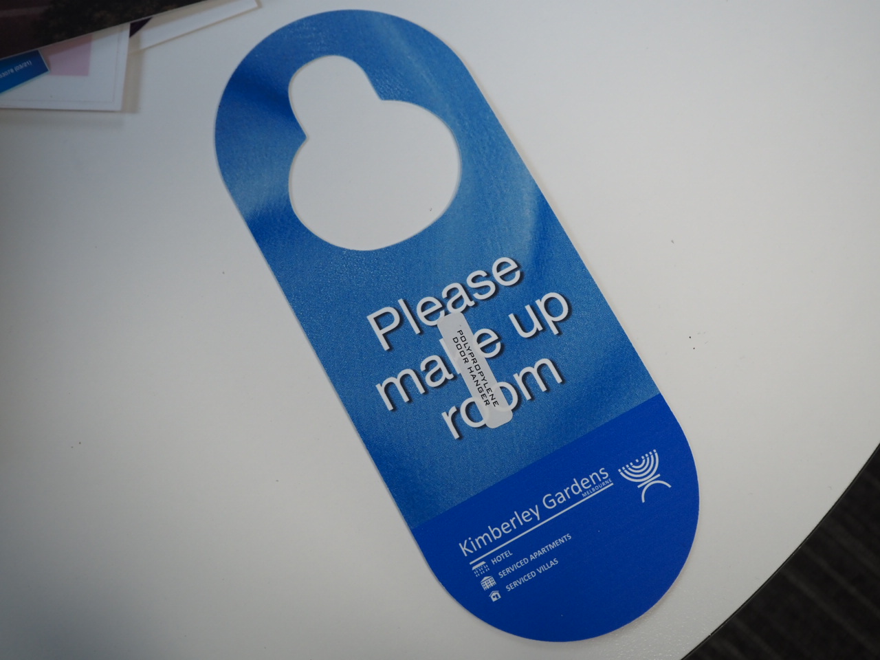 Blue door hanger on a table reads Please make up room with Melbourne's Kimberley Gardens logo.