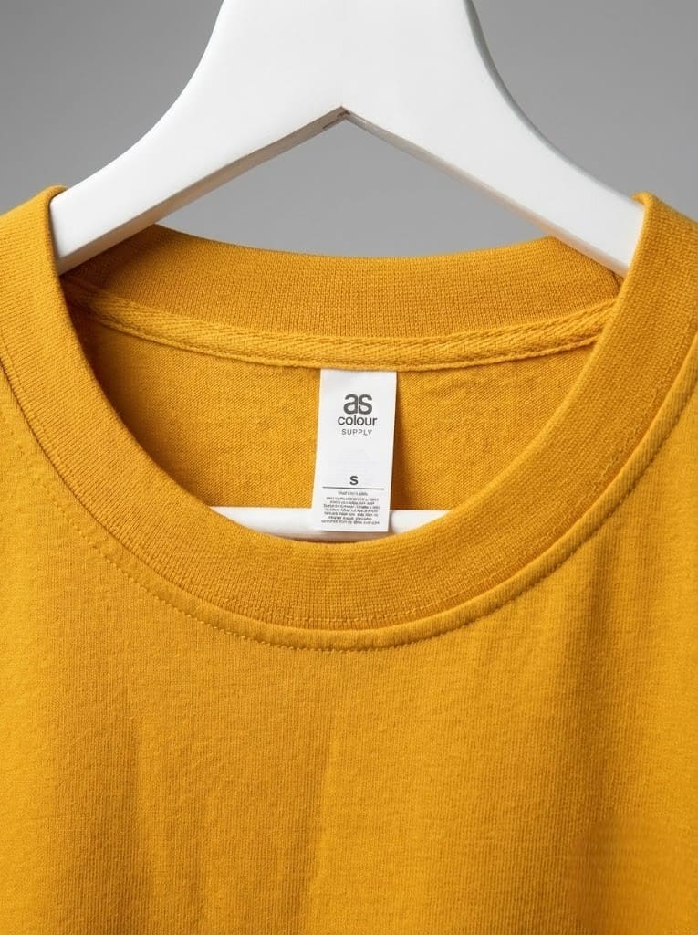 Close-up of a yellow t-shirt on a hanger, highlighting the collar and popular clothing brands label.