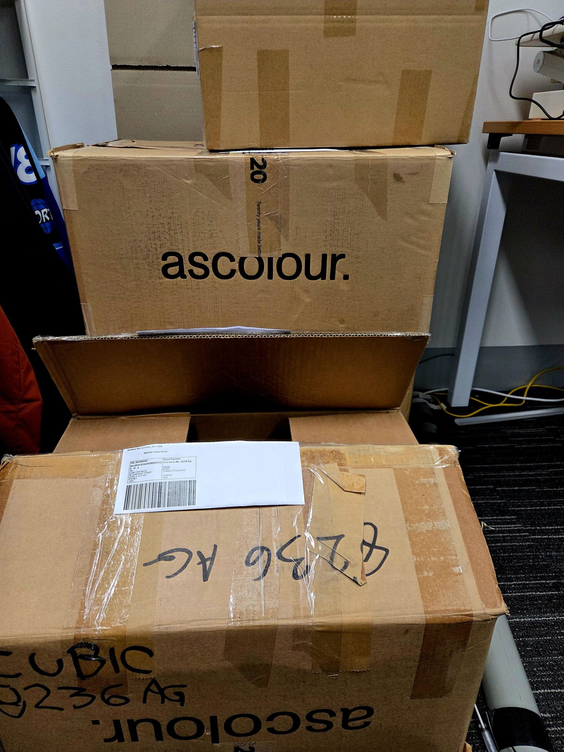 Four stacked cardboard boxes, one labeled ascolour, from a promotional products supplier.
