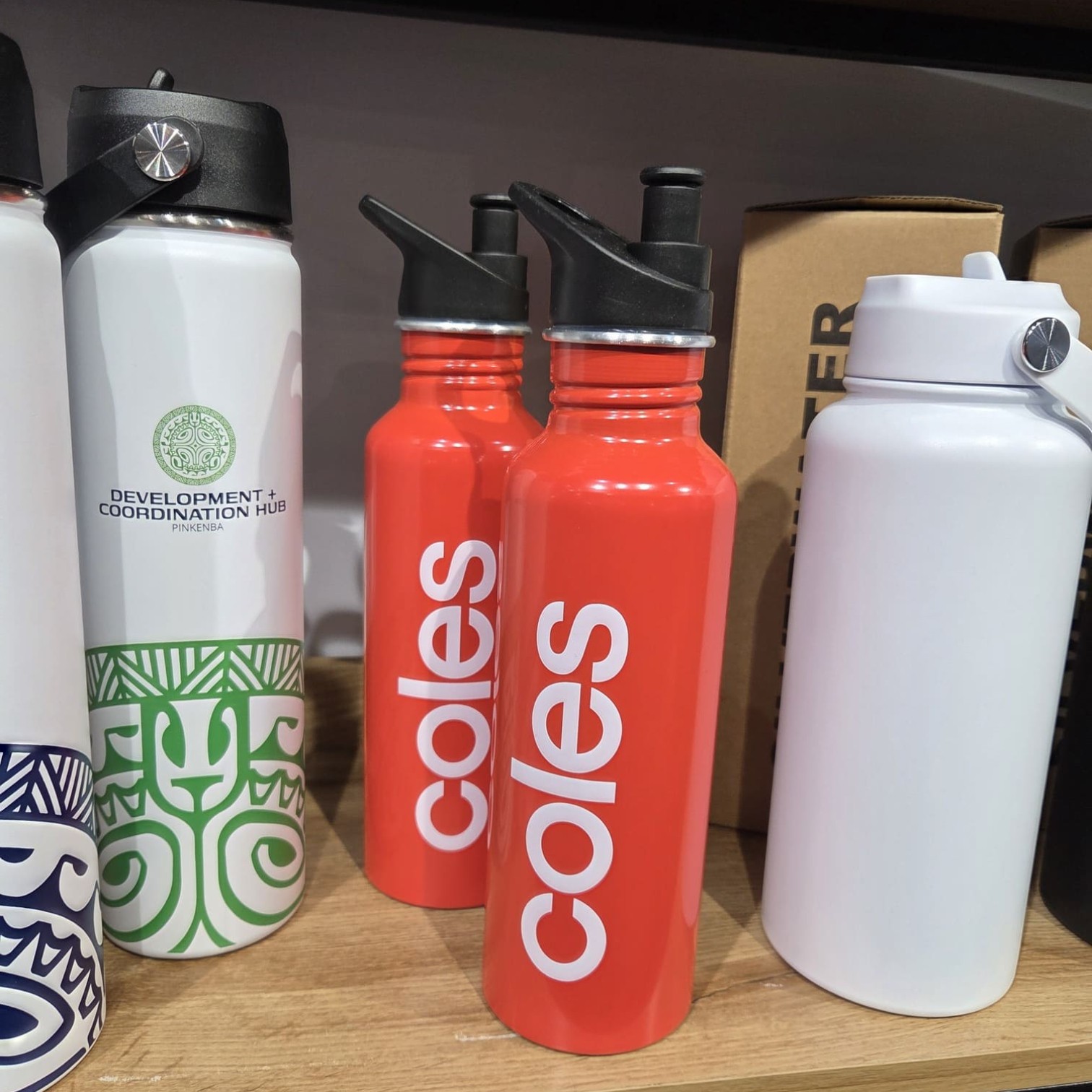 Red Coles water bottles with white branding on a shelf beside other water bottles.