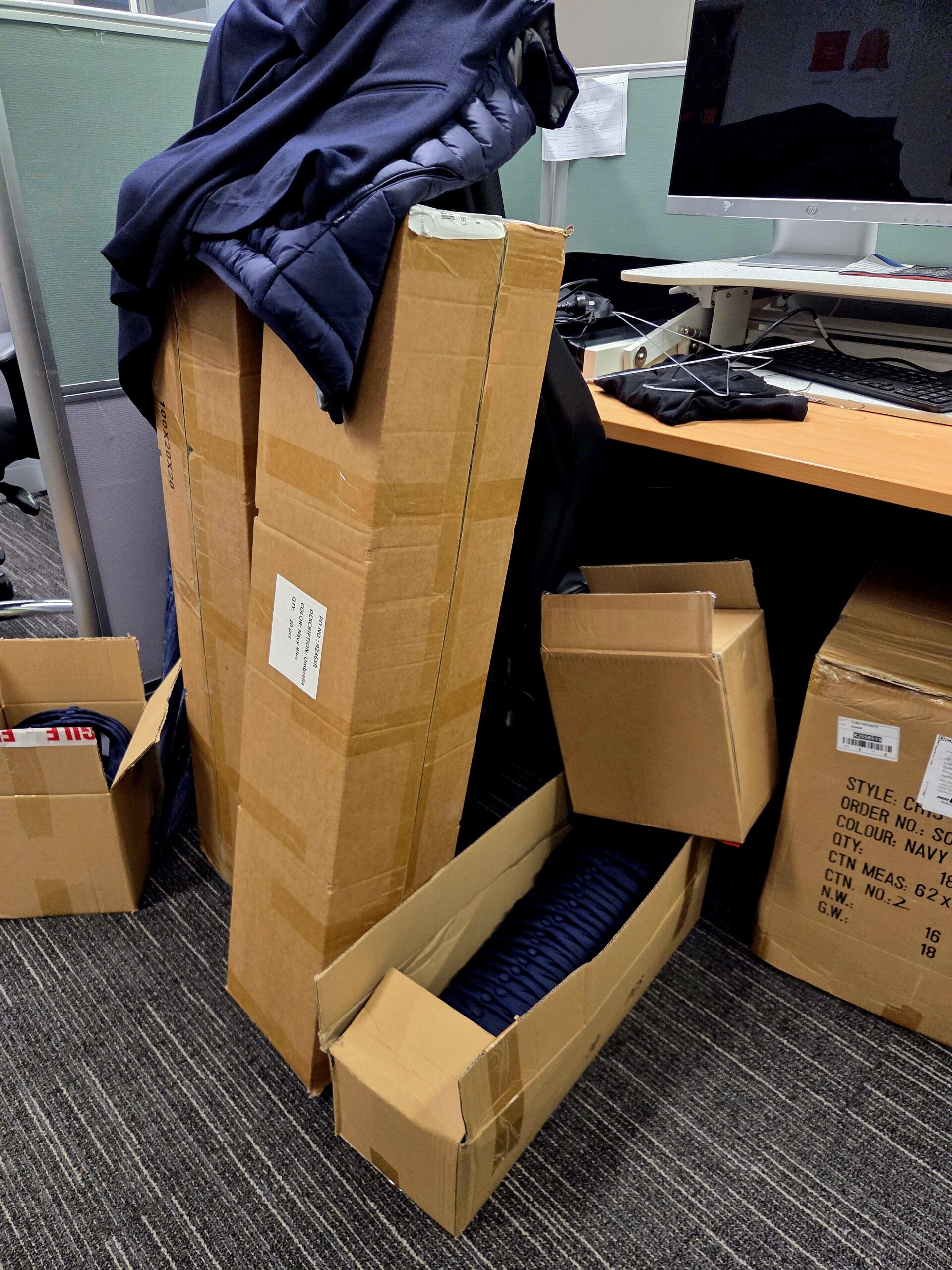 Several cardboard boxes from a promotional products supplier sit beside an office desk and computer.