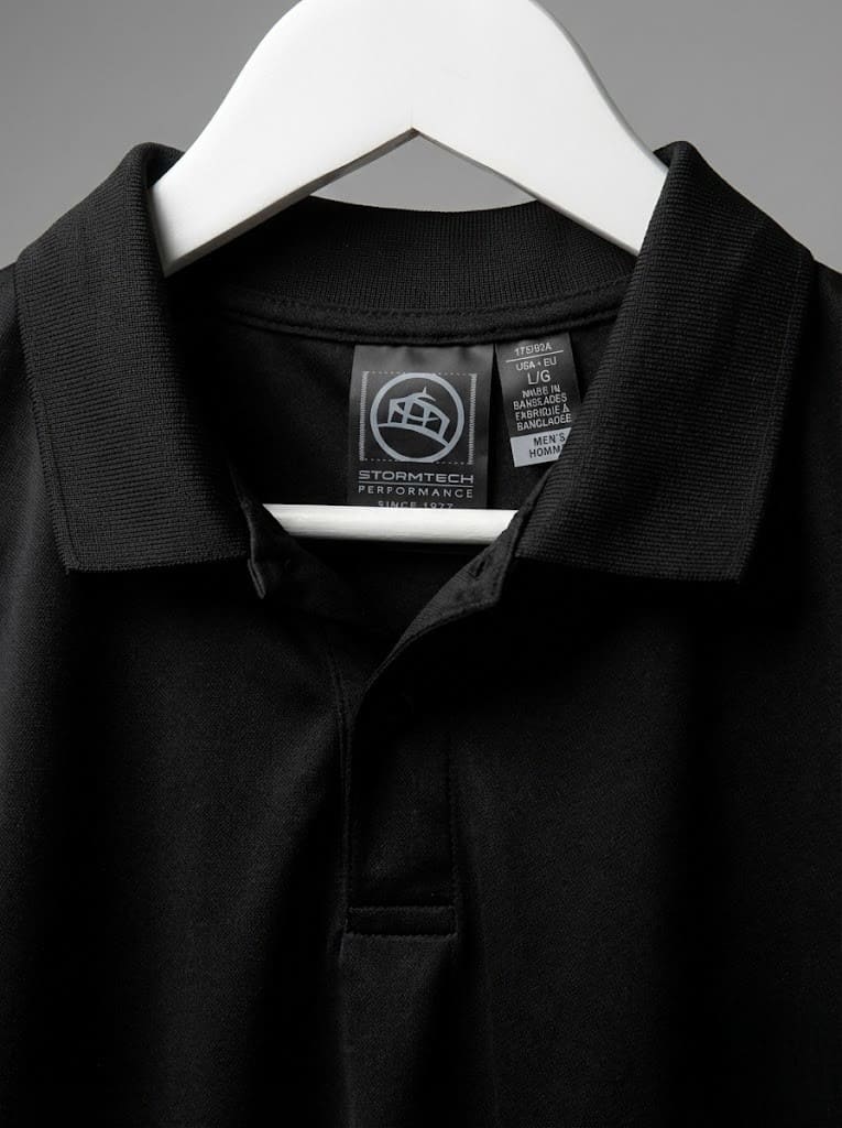 Close-up of a black polo shirt from top clothing brands on a white hanger with visible tags.