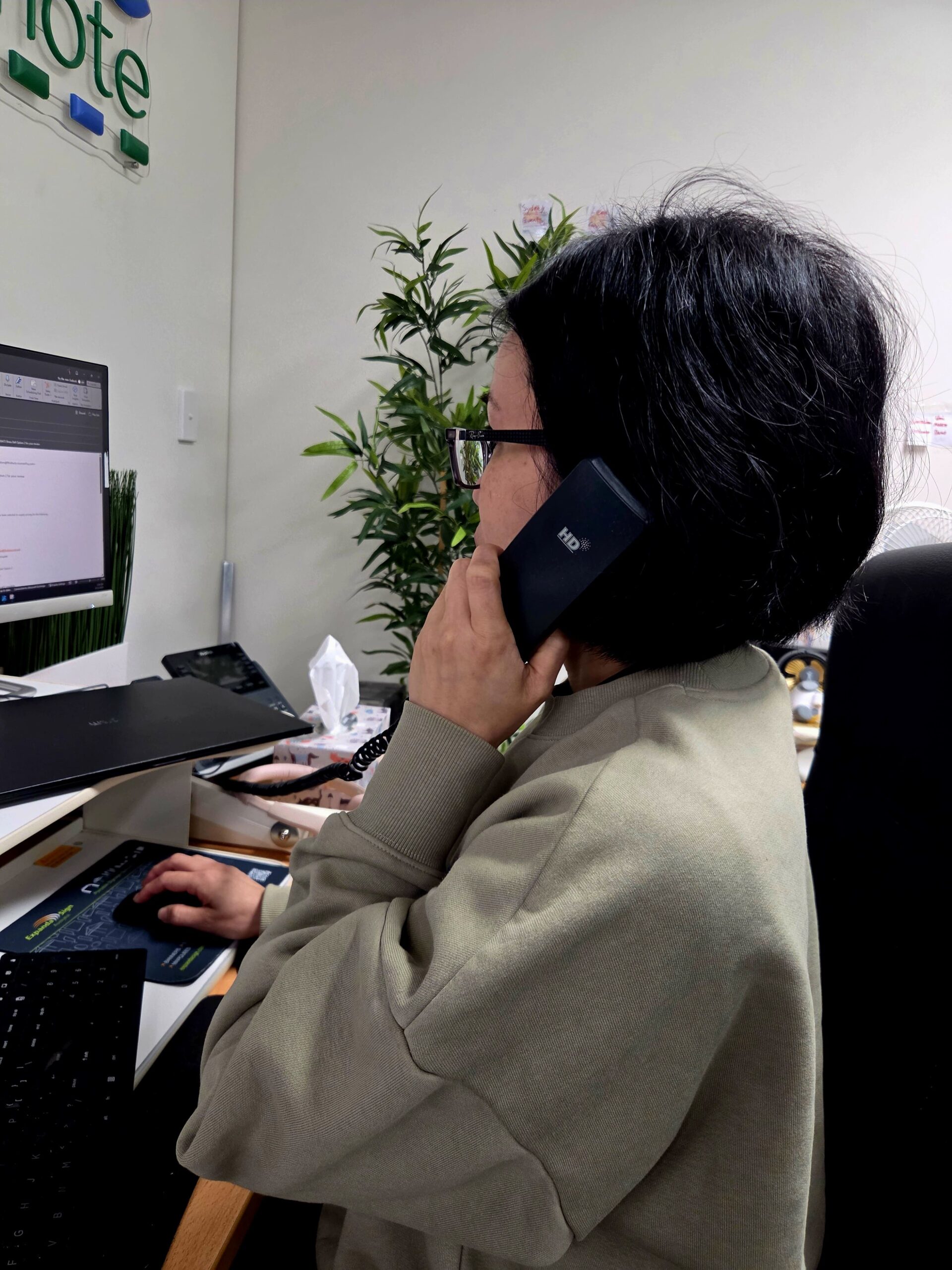 Woman in glasses at desk using computer mouse, talking on the phone with a promotional products supplier.