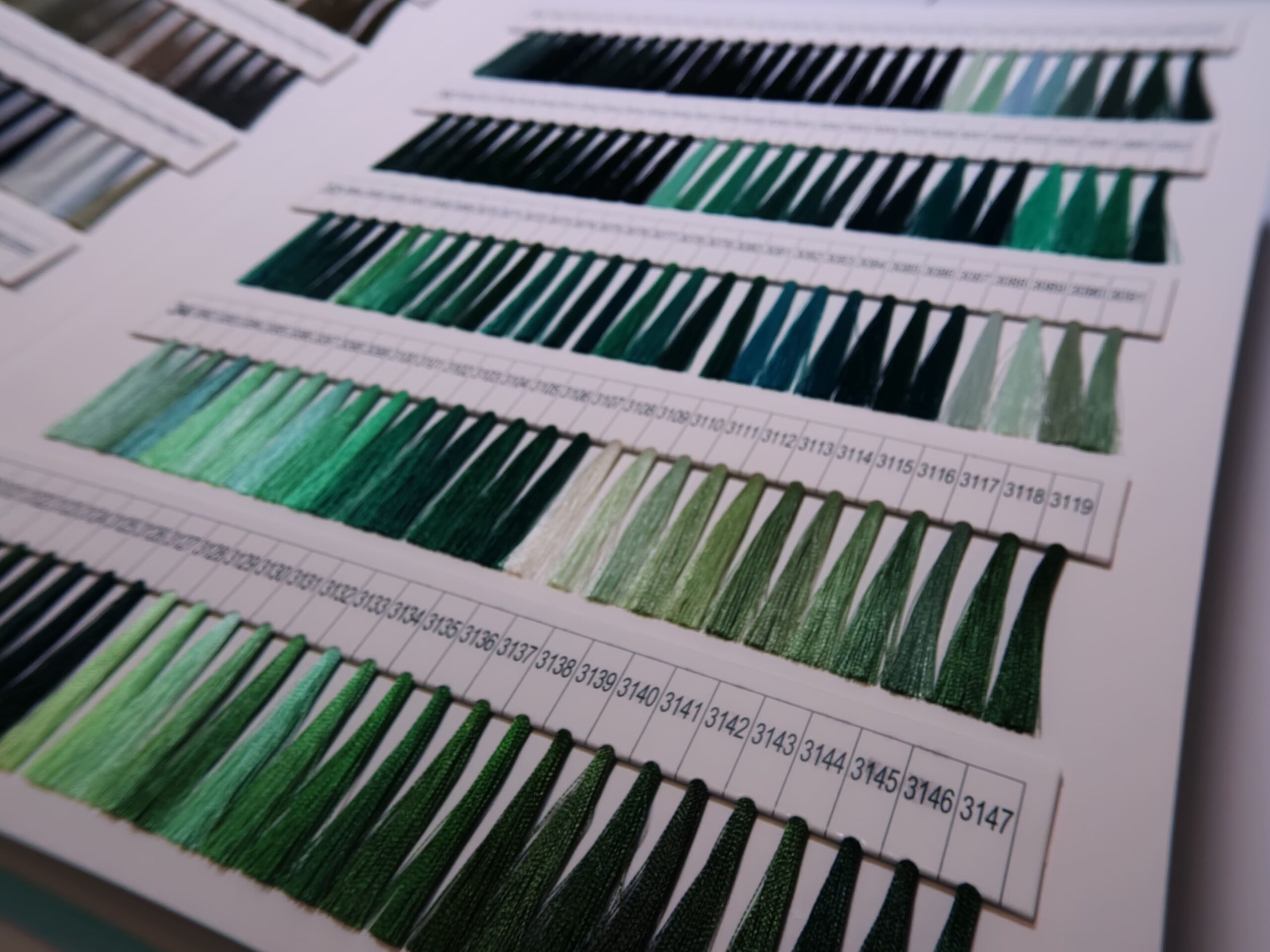Threads in various shades of green are displayed in rows on a showroom color chart.