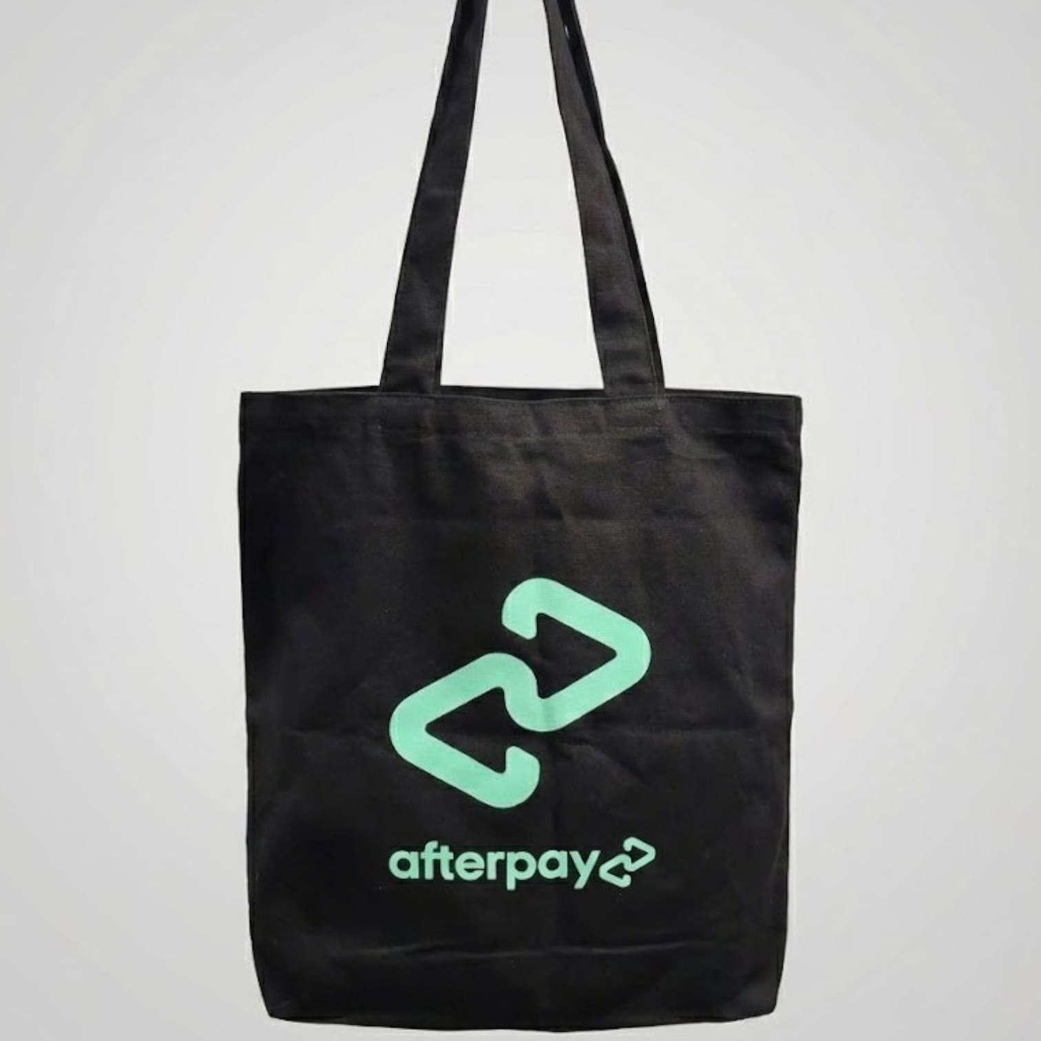 Black tote bag featuring the Afterpay logo and text in light green, reflecting product trends.