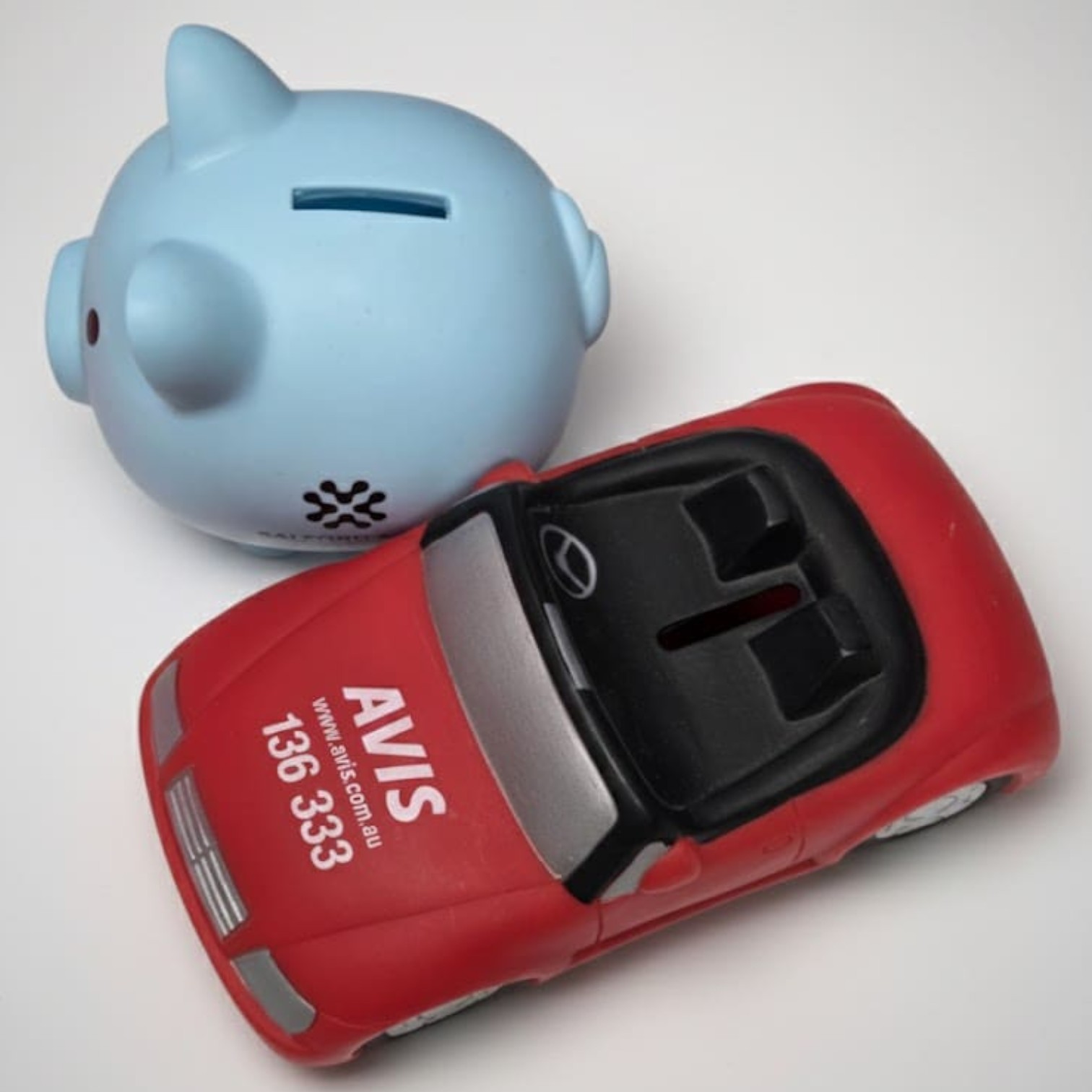 A blue piggy bank and a red toy car feature AVIS branding on a white background.