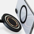 A magnetic wireless charger positioned near the back of a smartphone with a ring attachment.