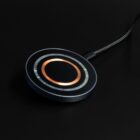 A round wireless charging pad with a copper coil on a black background.