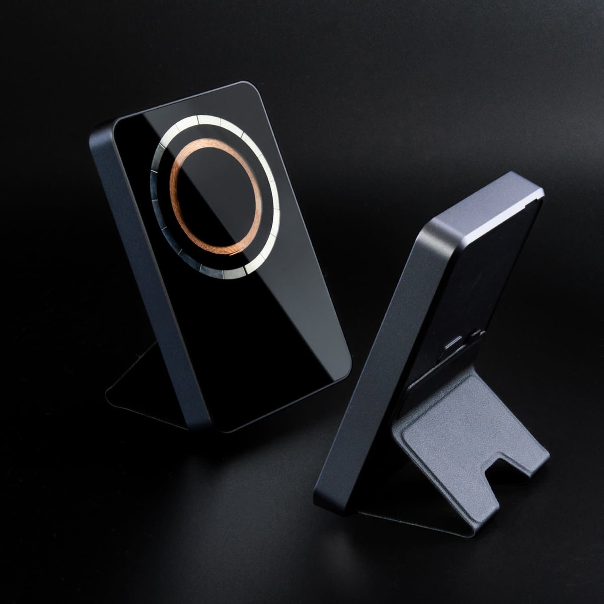 Two sleek, black wireless chargers with metallic rings, displayed on stands against a black background.