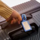A hand holding a suitcase handle with a blue luggage tag attached.